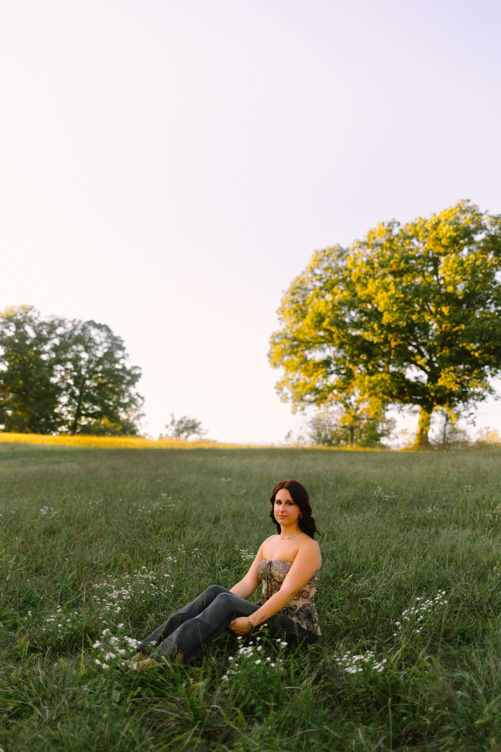 Person sits in a grassy meadow at sunset with golden trees and wildflowers in the background.