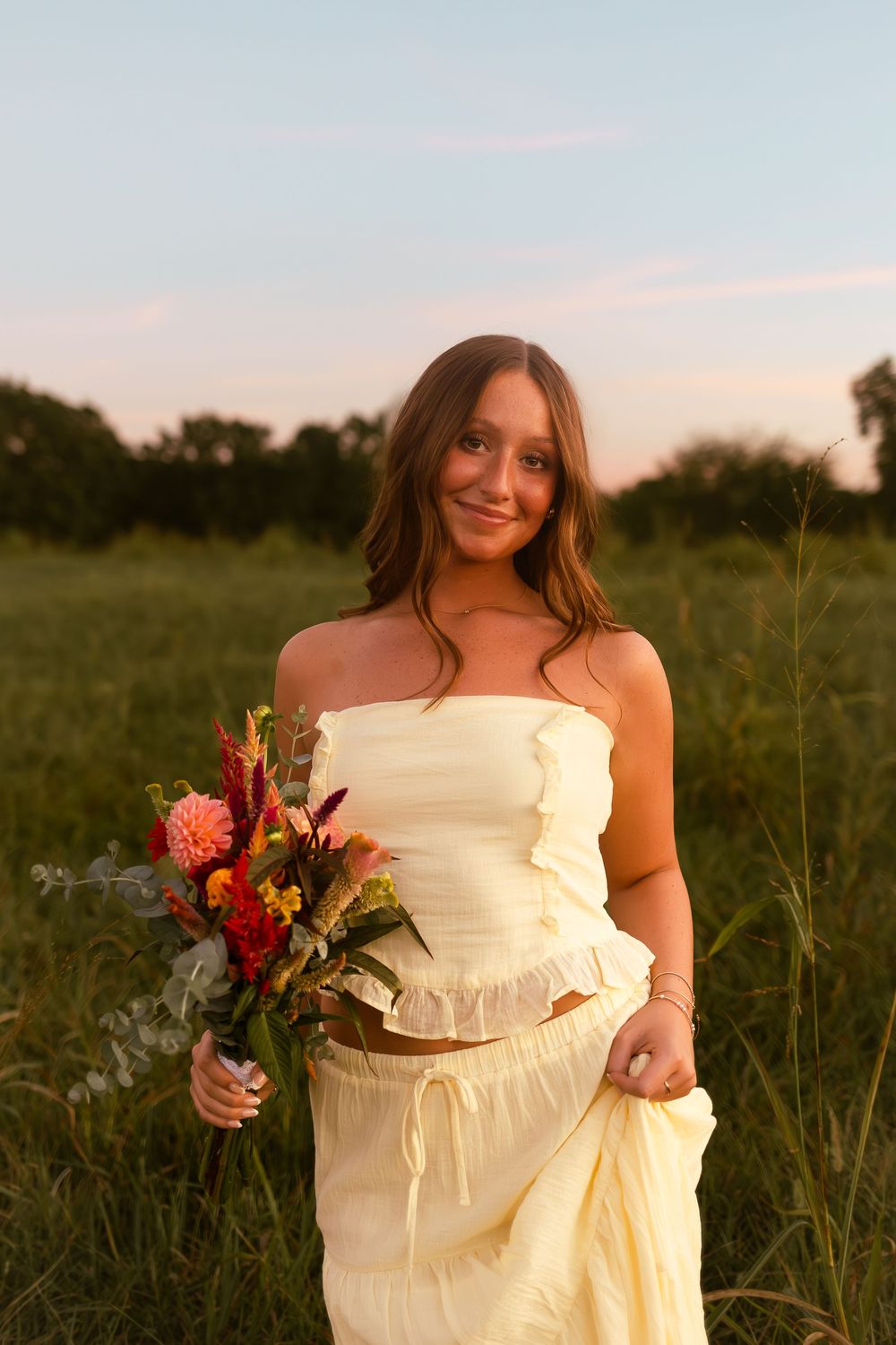 A person in a cream-colored dress holds a vibrant autumn bouquet while standing in a sunlit meadow at golden hour.
