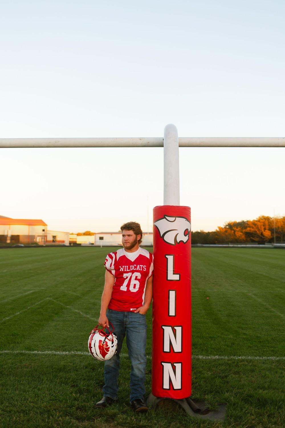 Family wearing red Nebraska Huskers jerseys poses together on a football field at sunset.