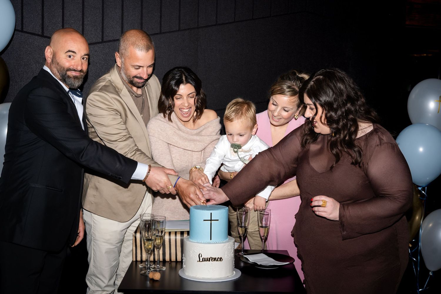 Family group photo at a christening ceremony with six adults and a baby near a baptismal font.