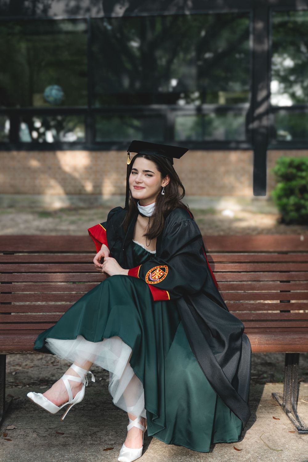 A young woman in an emerald green dress poses outdoors with her hair flowing in the wind.