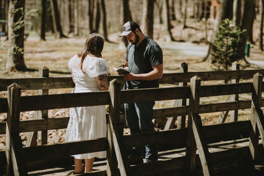 Couple sharing vows on a wooden bridge surrounded by trees in a forest wedding ceremony.