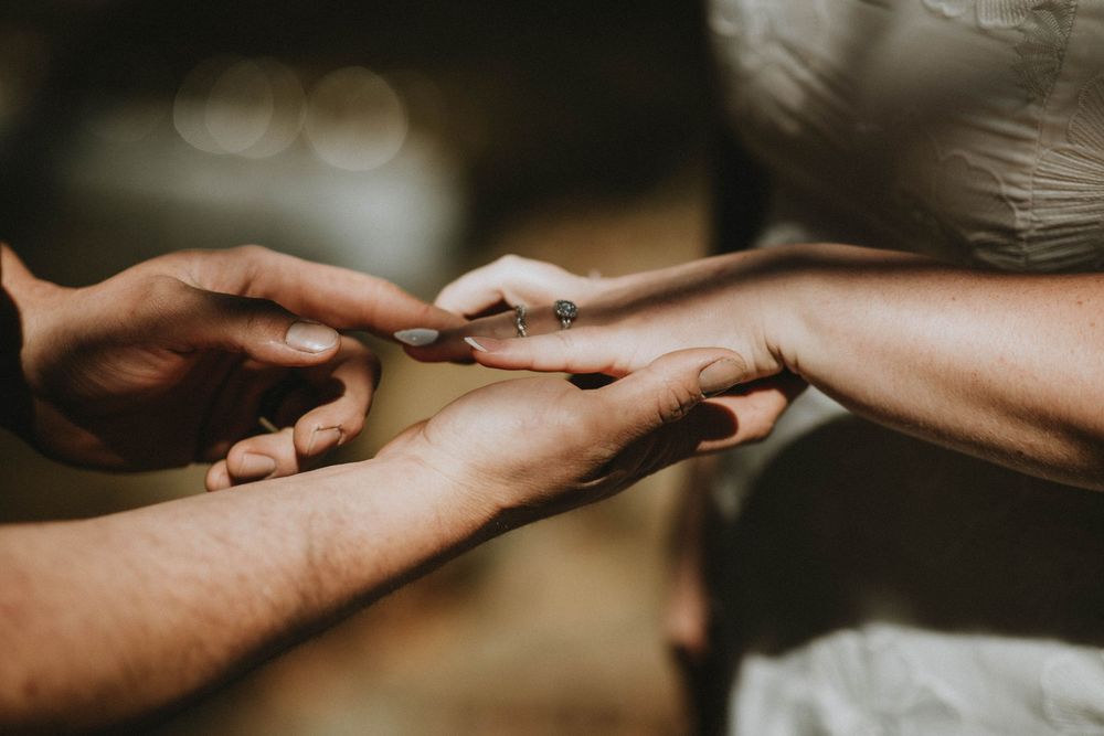 Close-up of two people gently holding hands, one wearing a ring, in a romantic outdoor setting.