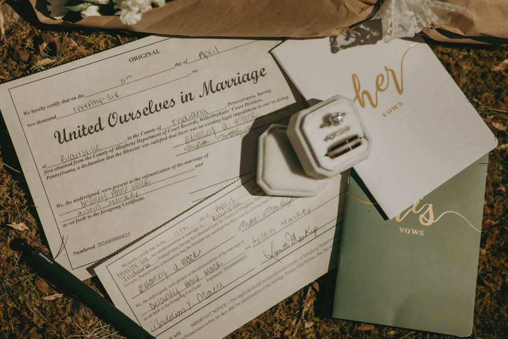 Wedding marriage certificate with rings, her and his vow books displayed on grass at an outdoor wedding ceremony.