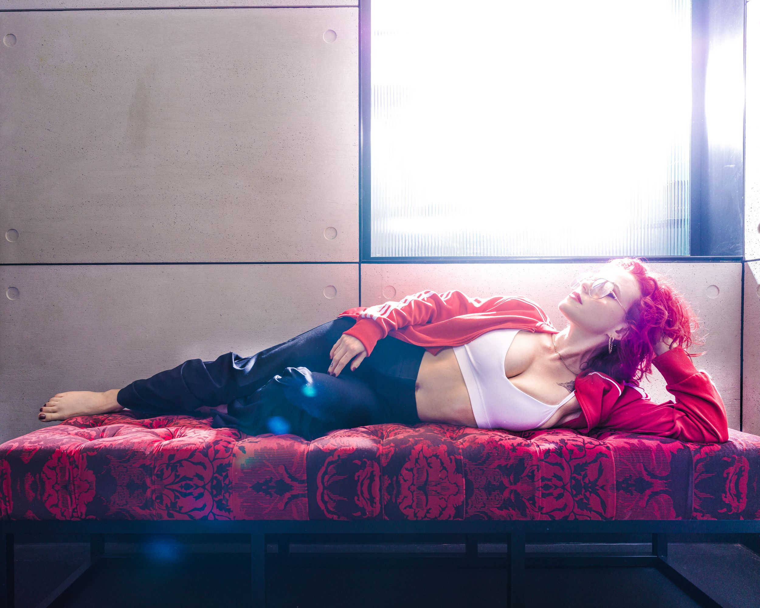 Editorial portrait of a model with red hair lying on a red patterned chaise lounge