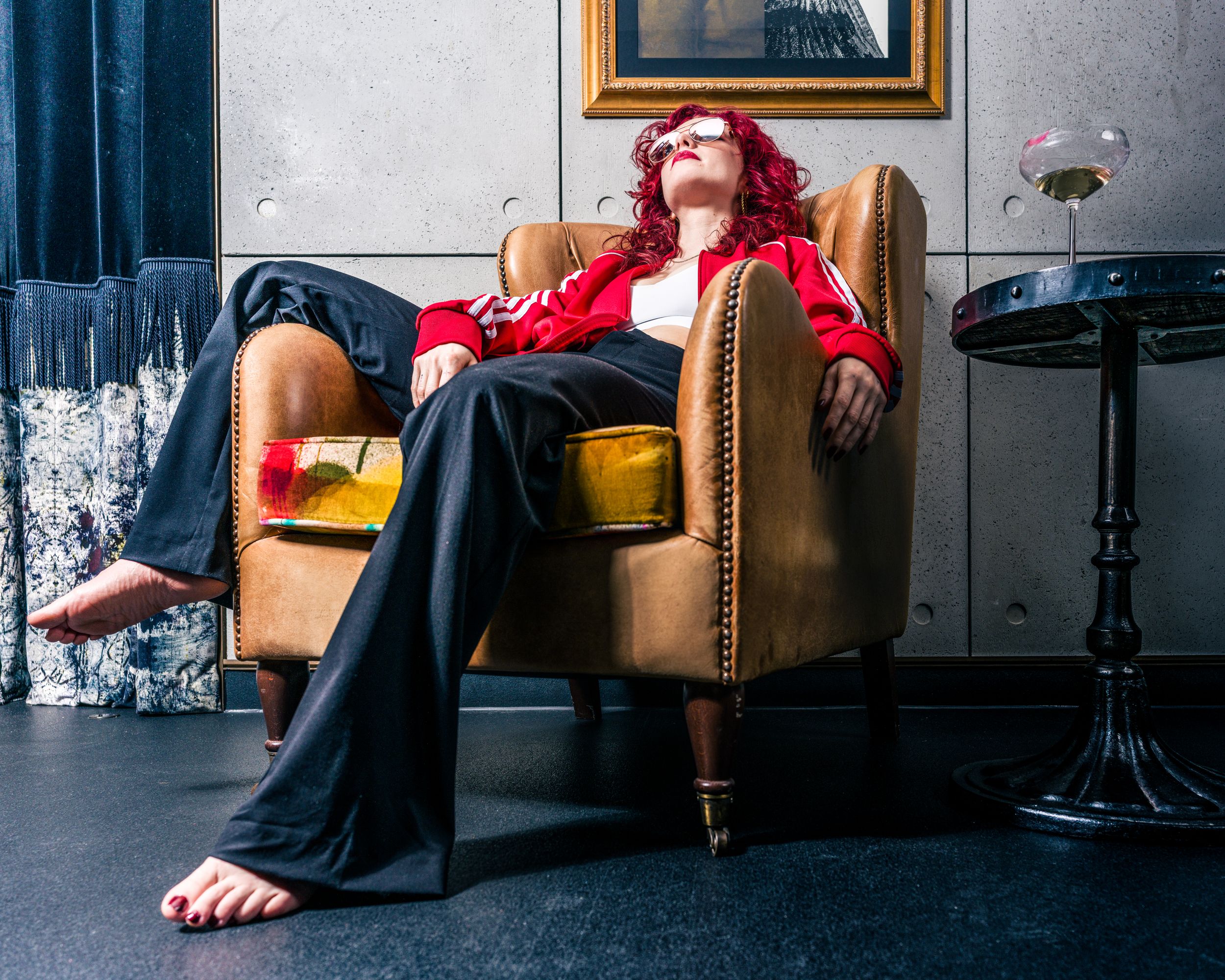 Editorial portrait of a model with red hair in a red blazer reclining in a gold armchair