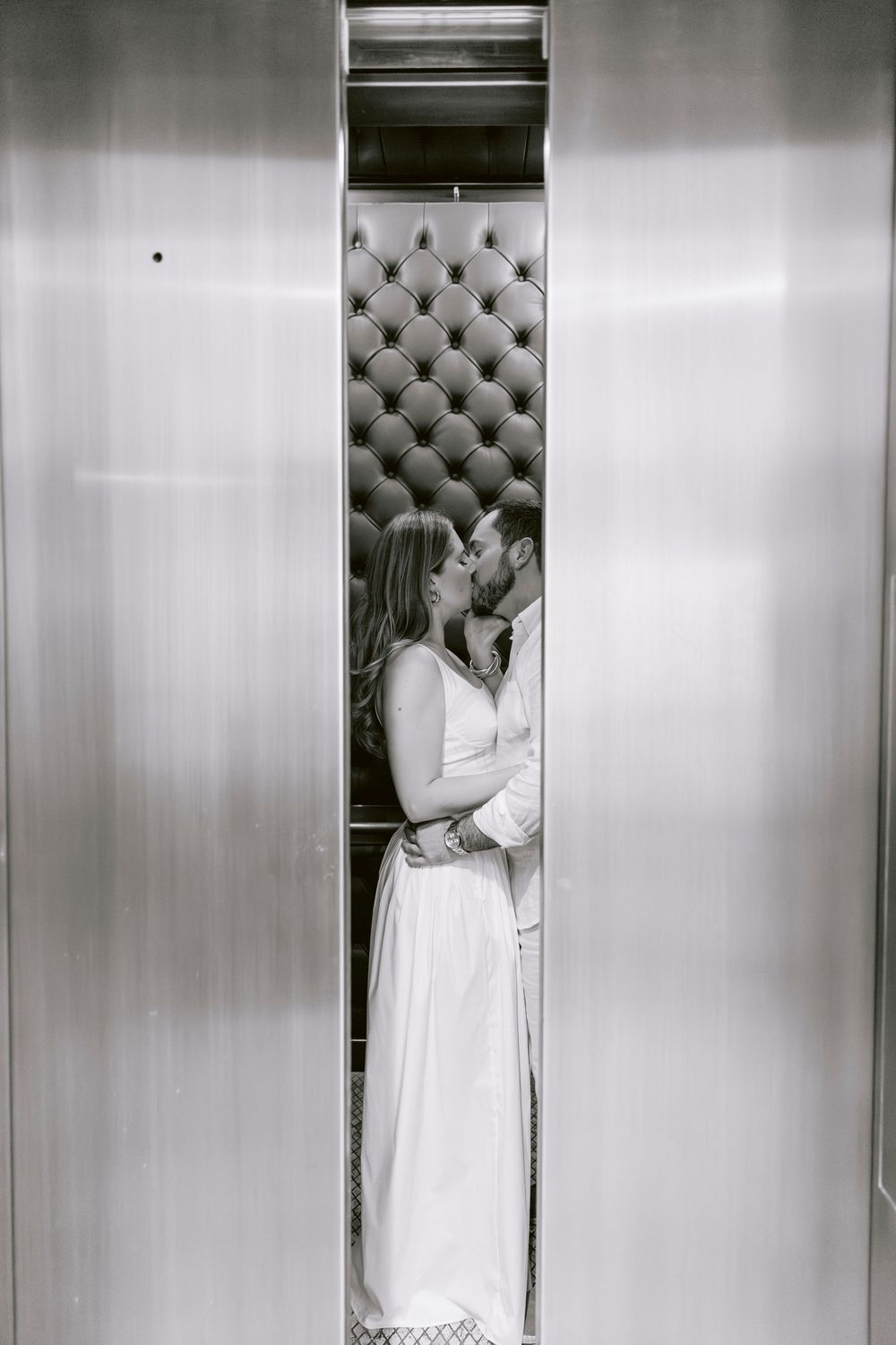 Black and white photo of couple kissing in elevator with tufted velvet interior.