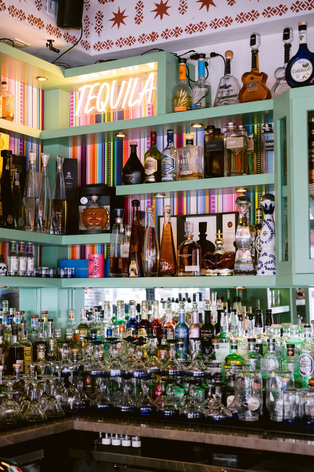 Tequila bar with colorful shelves stocked with bottles, neon sign, and vibrant striped backdrop.