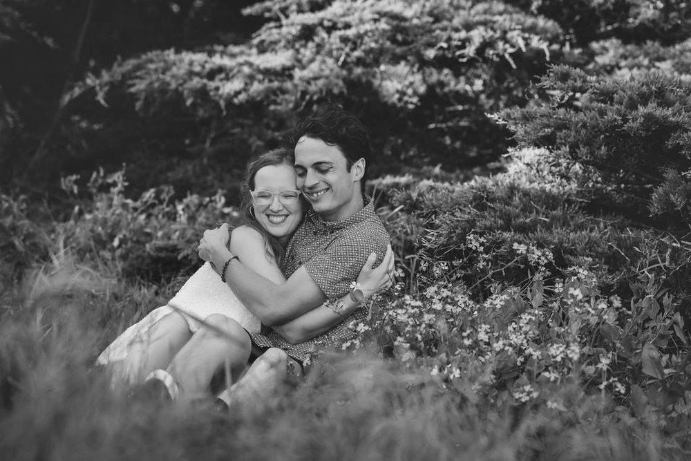 Happy couple embracing and smiling while sitting together in a lush green meadow, black and white photo.