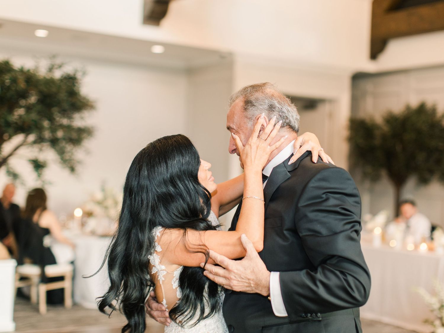 Bride and father sharing an emotional first dance at elegant wedding reception with soft lighting.