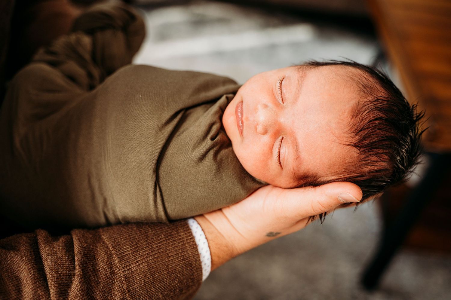 Mississauga lifestyle newborn photographer captures newborn baby swaddled in green being held gently in Dad's hands.