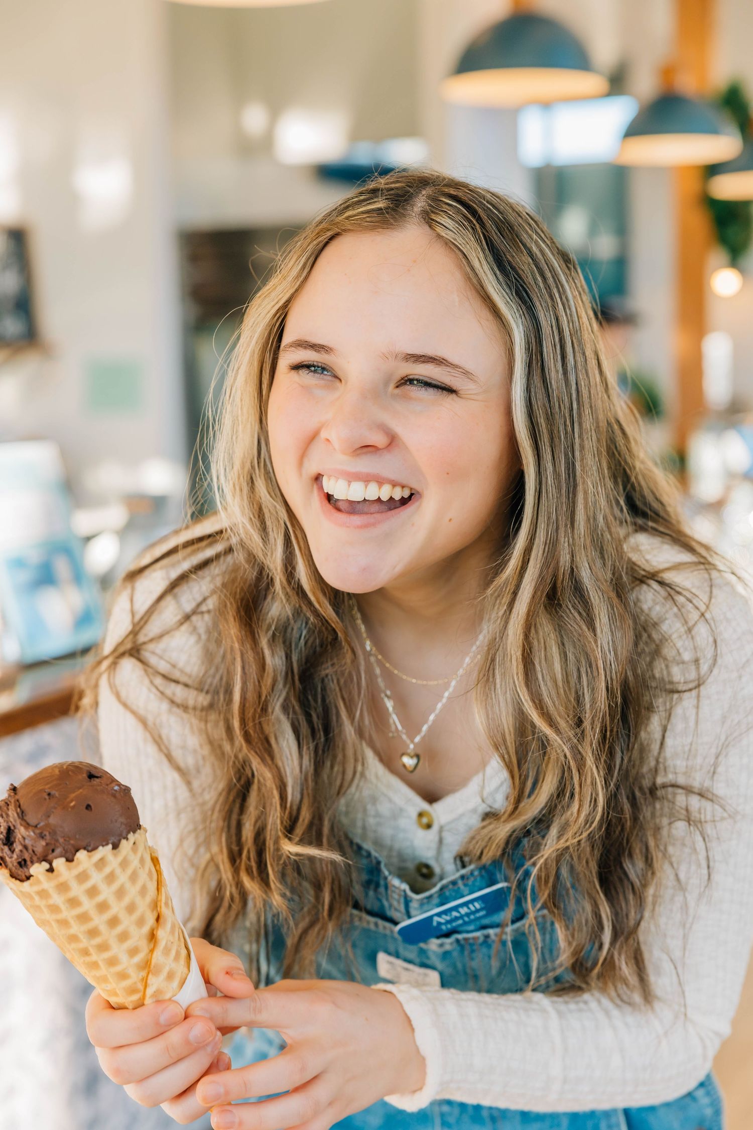 Happy teenage girl laughing while holding chocolate ice cream waffle cone indoors.