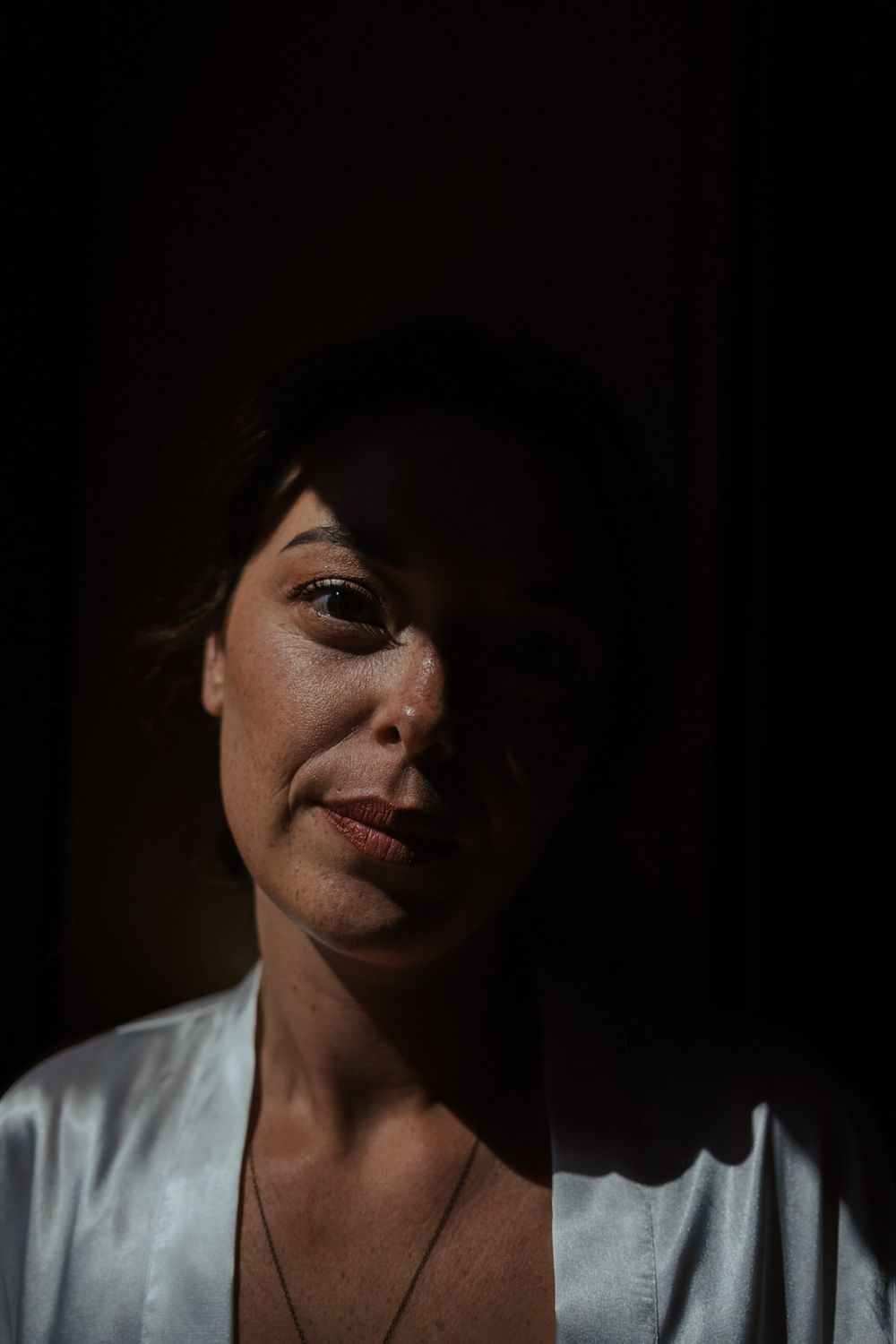 A woman in a white robe is dramatically lit by shadows, with half her face illuminated in a dark setting.