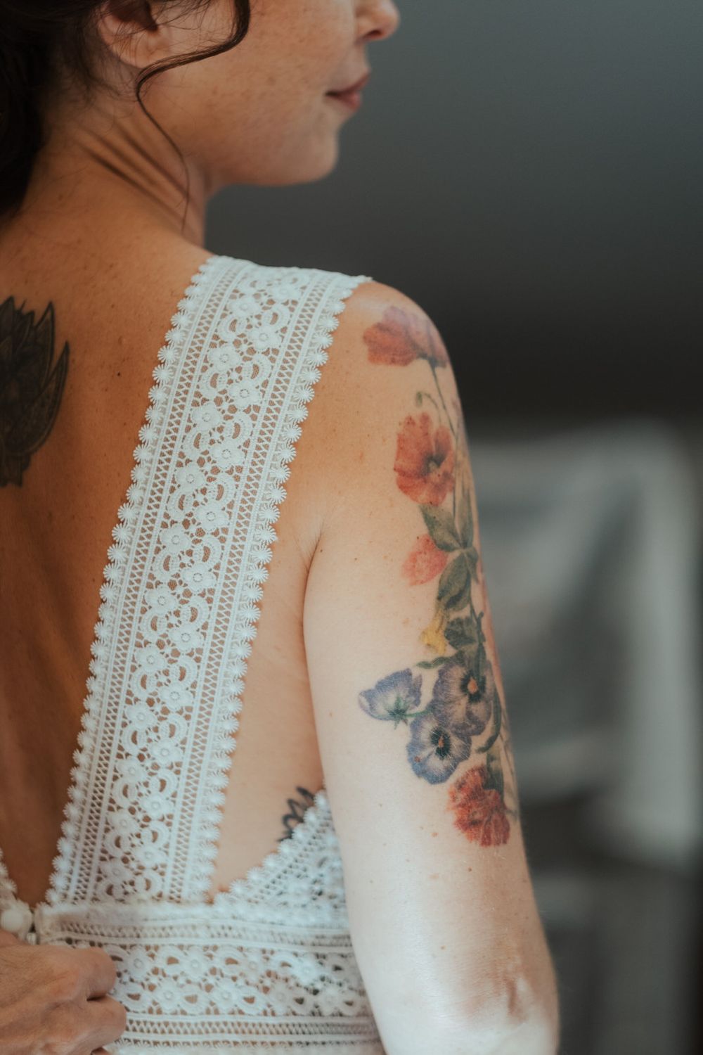Woman in white lace backless dress showcasing colorful floral and butterfly tattoo on her arm and shoulder.