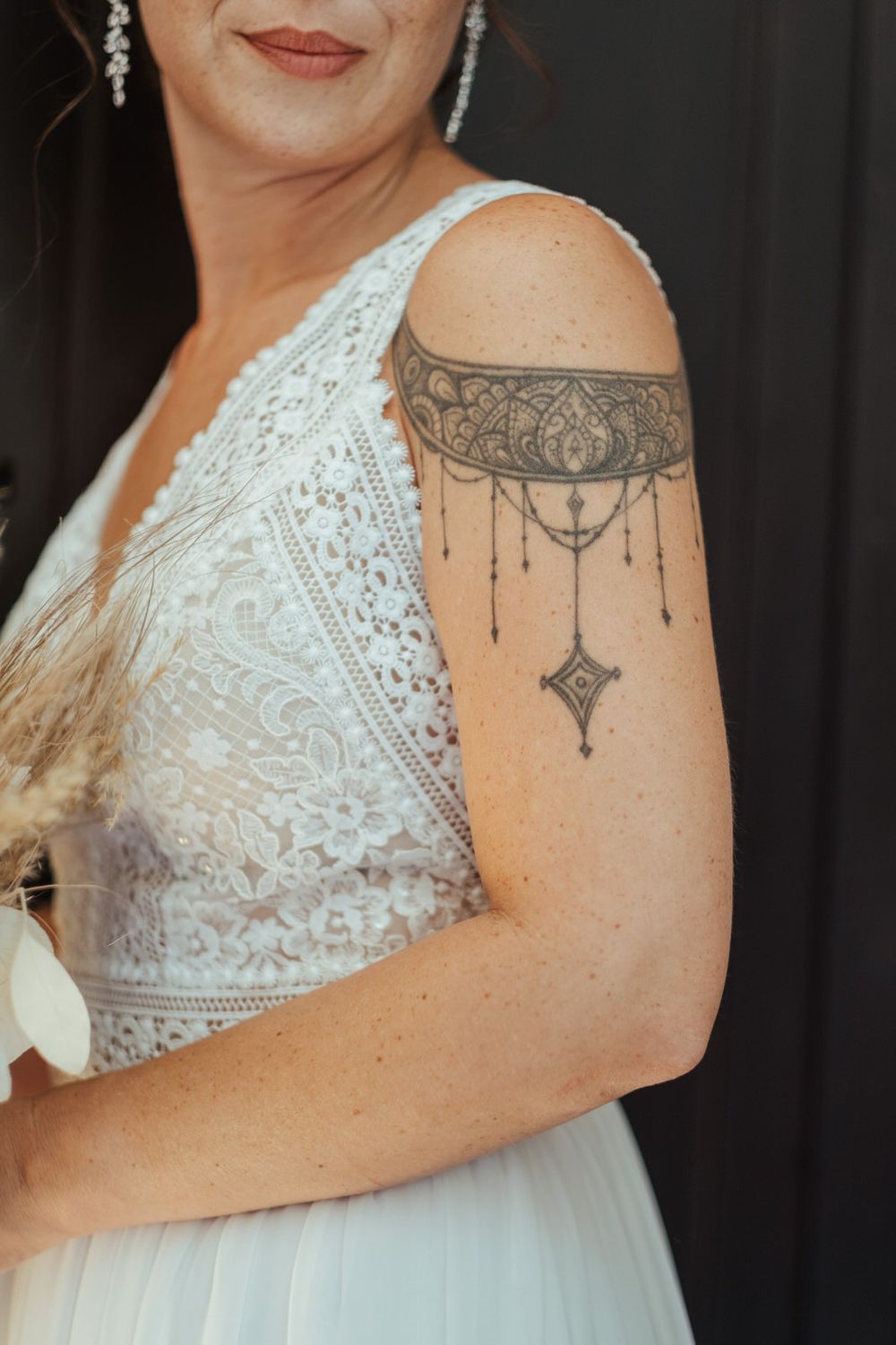 Bride in white lace wedding dress showcasing an ornate mandala upper arm tattoo with chandelier design.