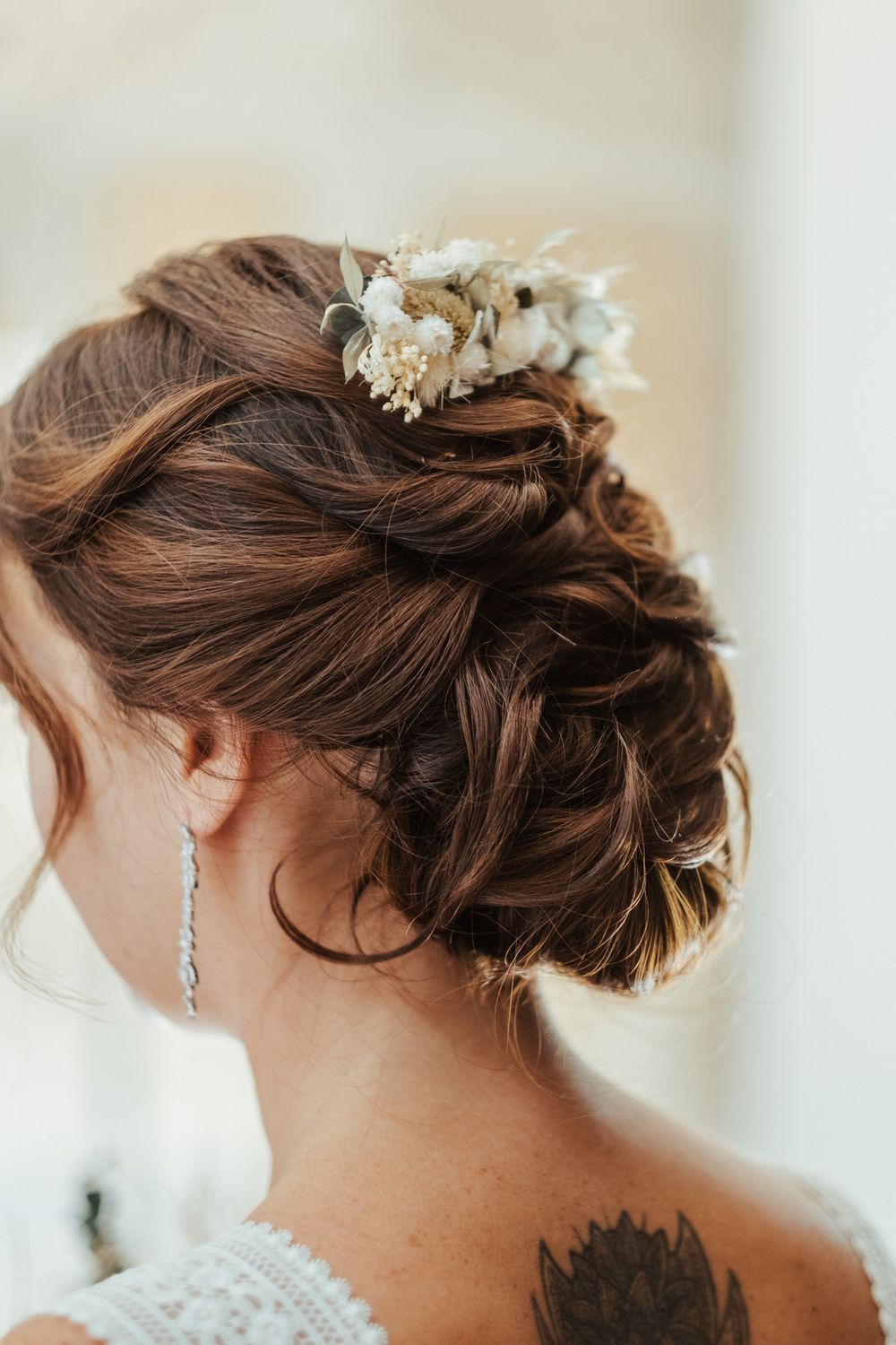 Elegant bridal updo with dried flower hair accessory and crystal drop earring, showcasing intricate twisted hairstyle.