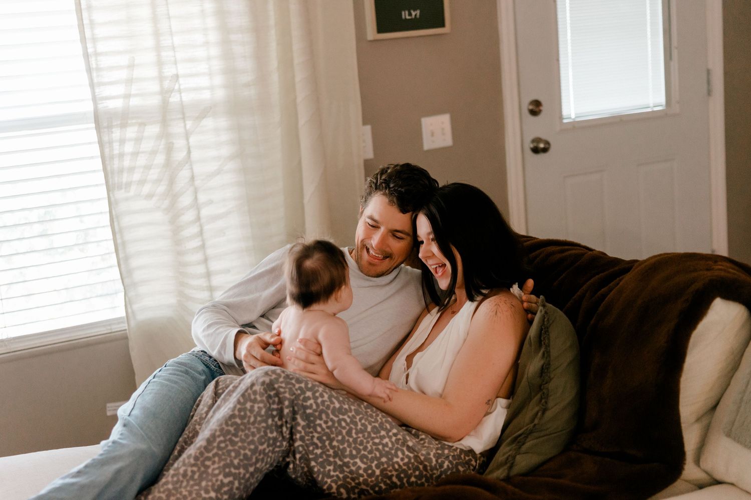 Happy young couple sitting on couch smiling at their newborn baby in a cozy home setting.