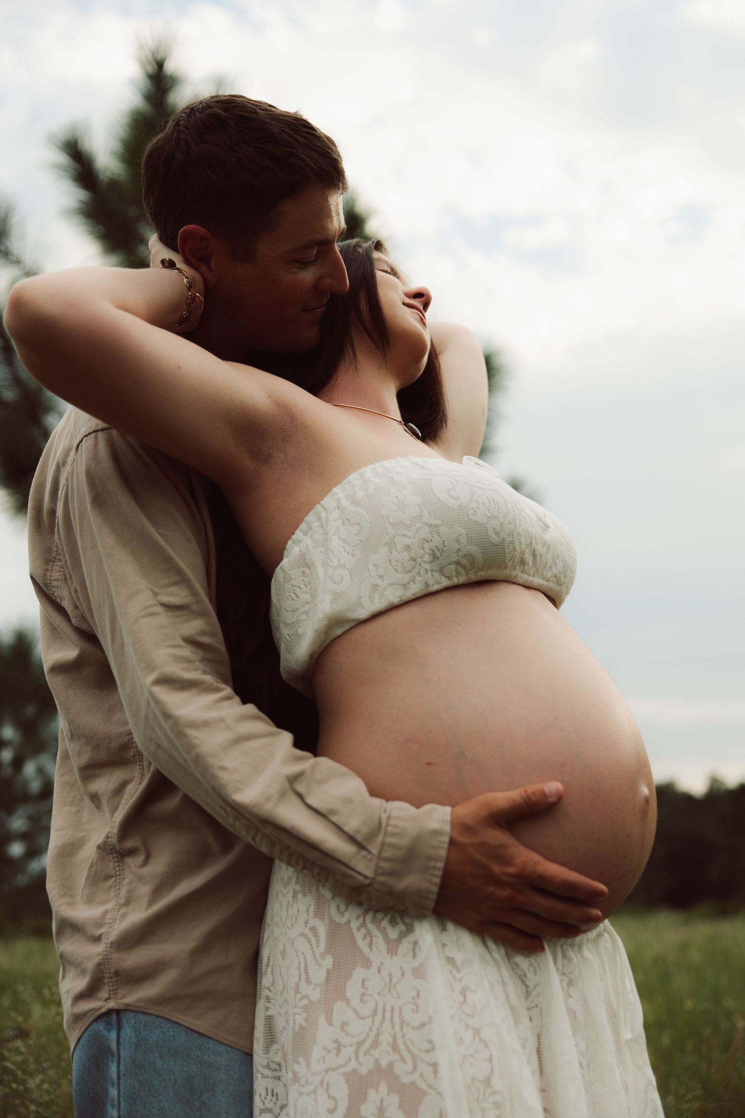 A man tenderly embraces a pregnant woman outdoors, cradling her bare belly in a romantic maternity photo.