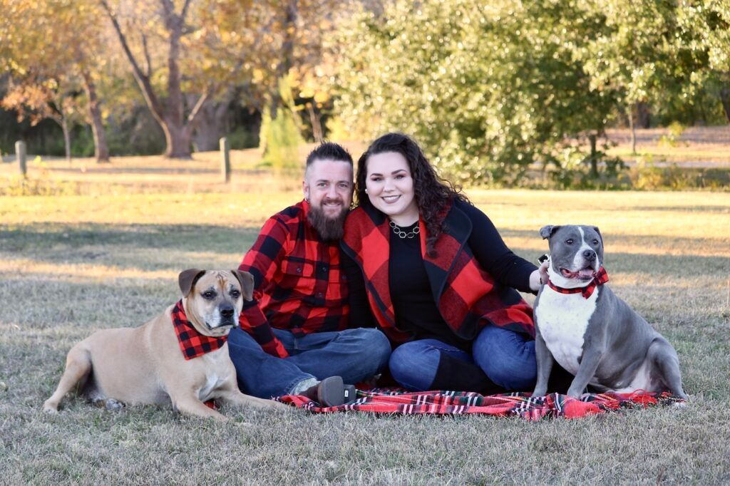 Couple seated on a blanket with their two dogs in a park