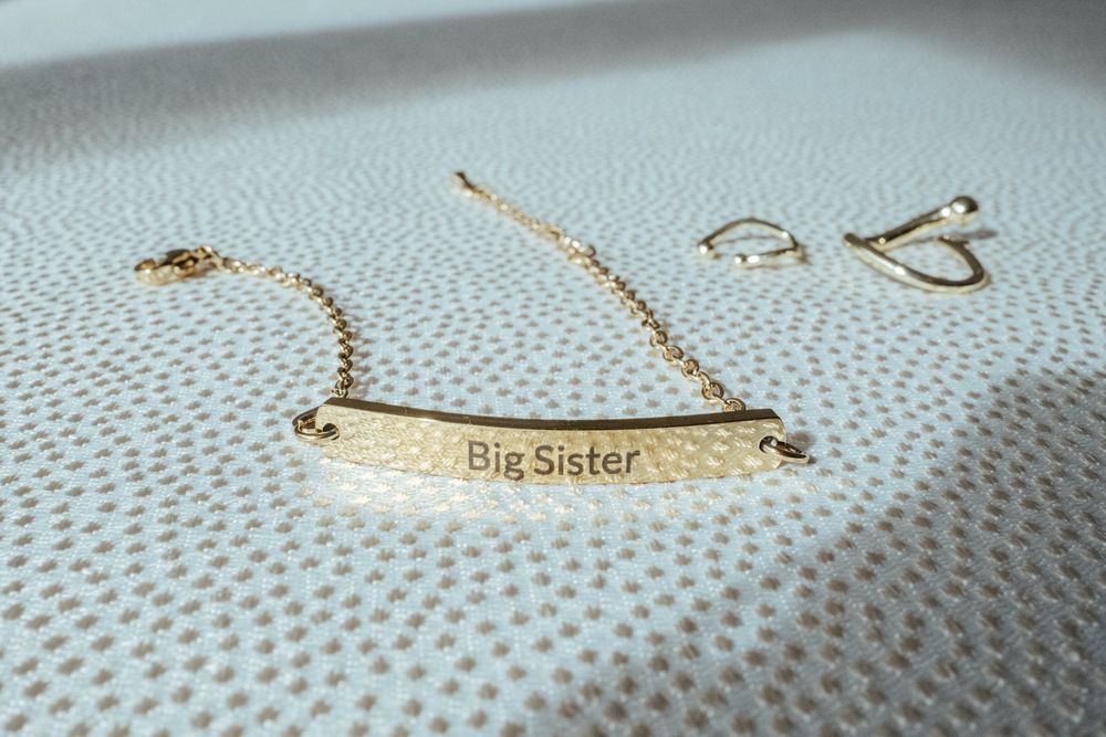 Gold 'Big Sister' engraved bar bracelet with delicate chain, displayed on white textured surface.