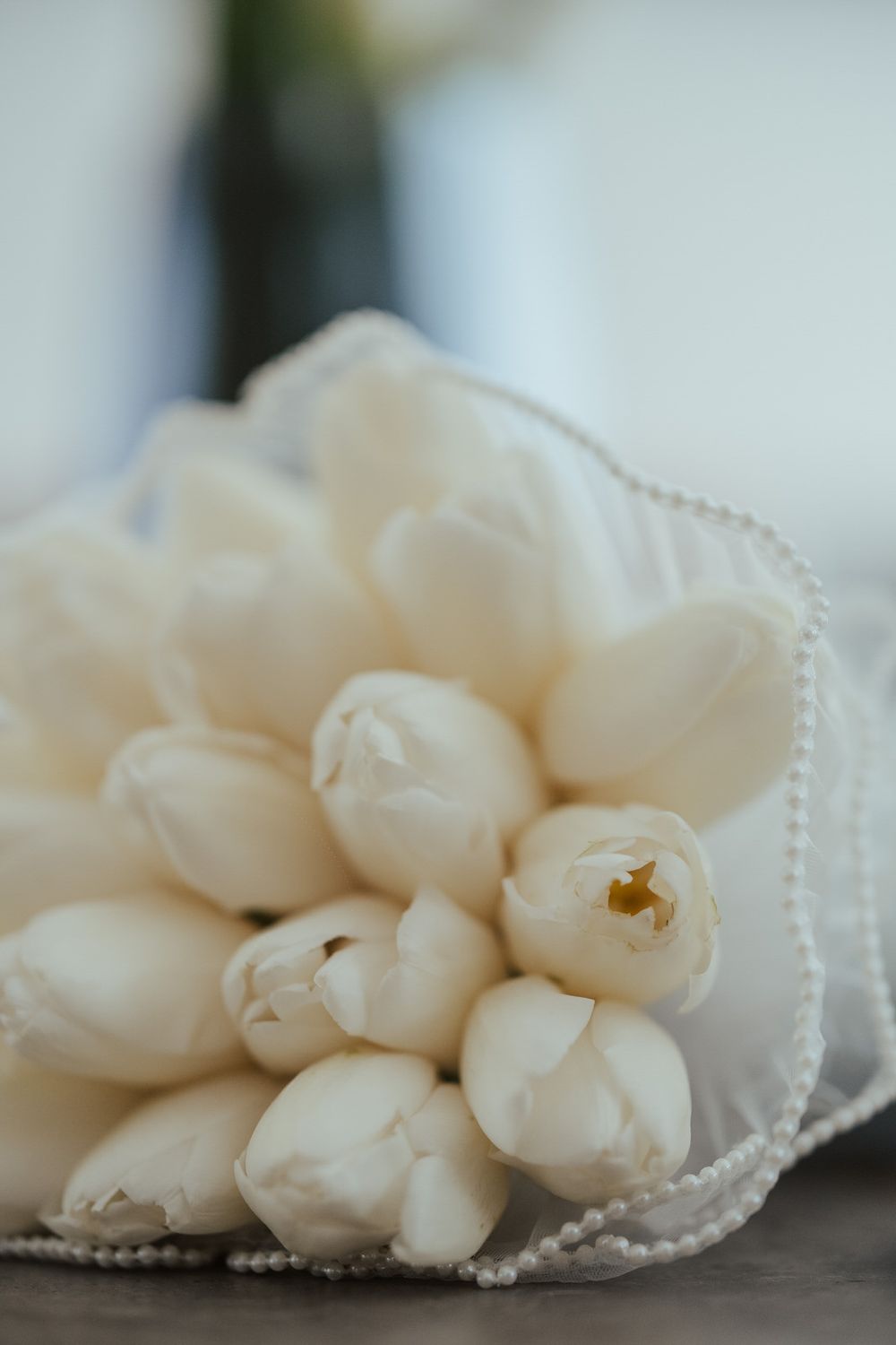 Close-up of a bridal bouquet of white tulips wrapped in white ribbon with pearl accents.