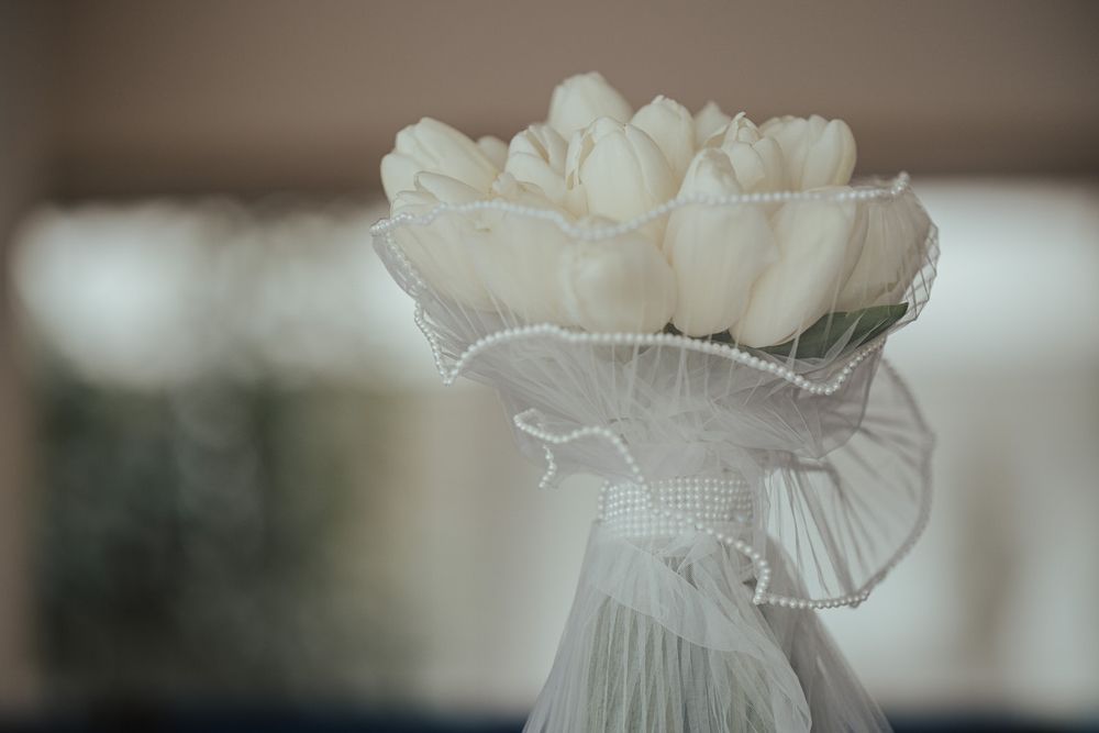 White tulip bridal bouquet wrapped in delicate tulle and pearl trim, elegant wedding flowers in soft focus.