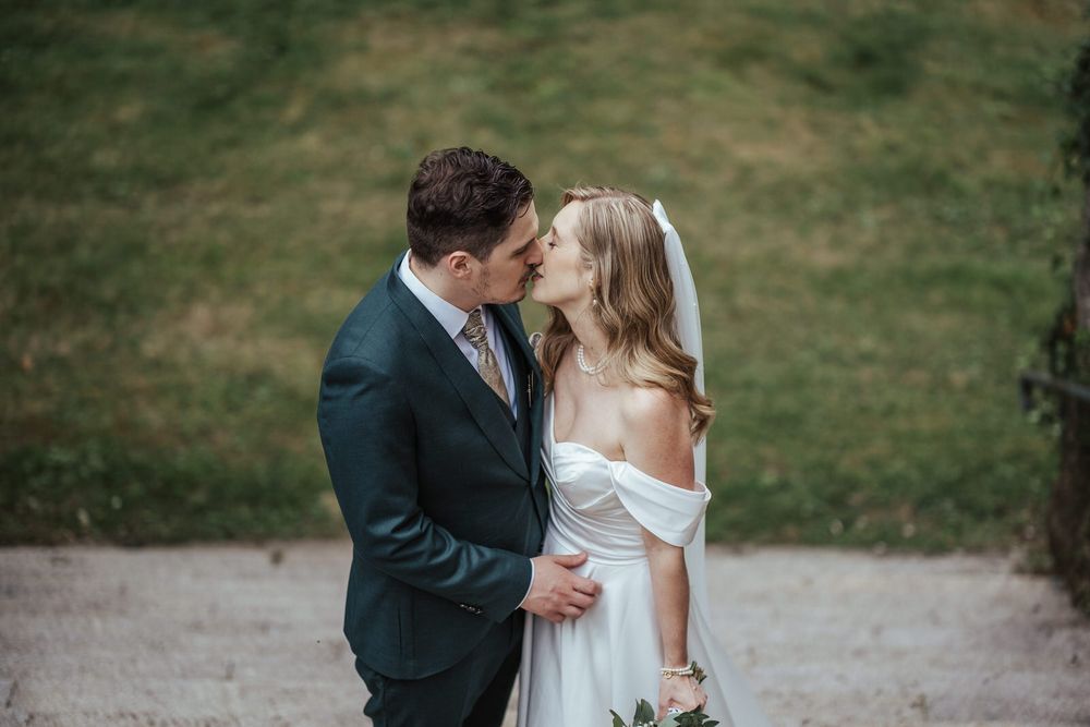 Bride and groom sharing a romantic kiss outdoors on their wedding day, with lush green grass in the background.