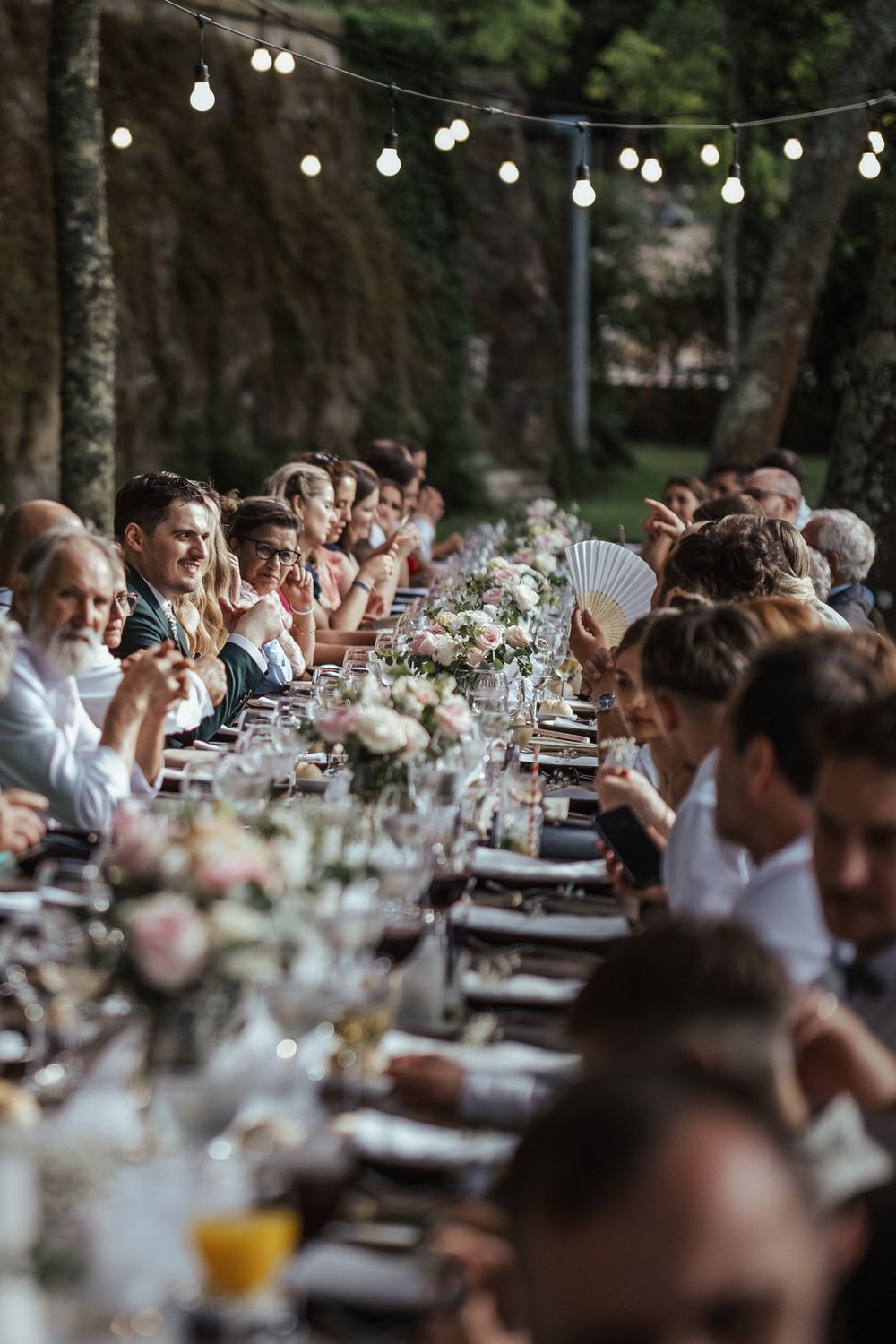 Elegant outdoor wedding reception with long decorated table, string lights, and floral centerpieces.