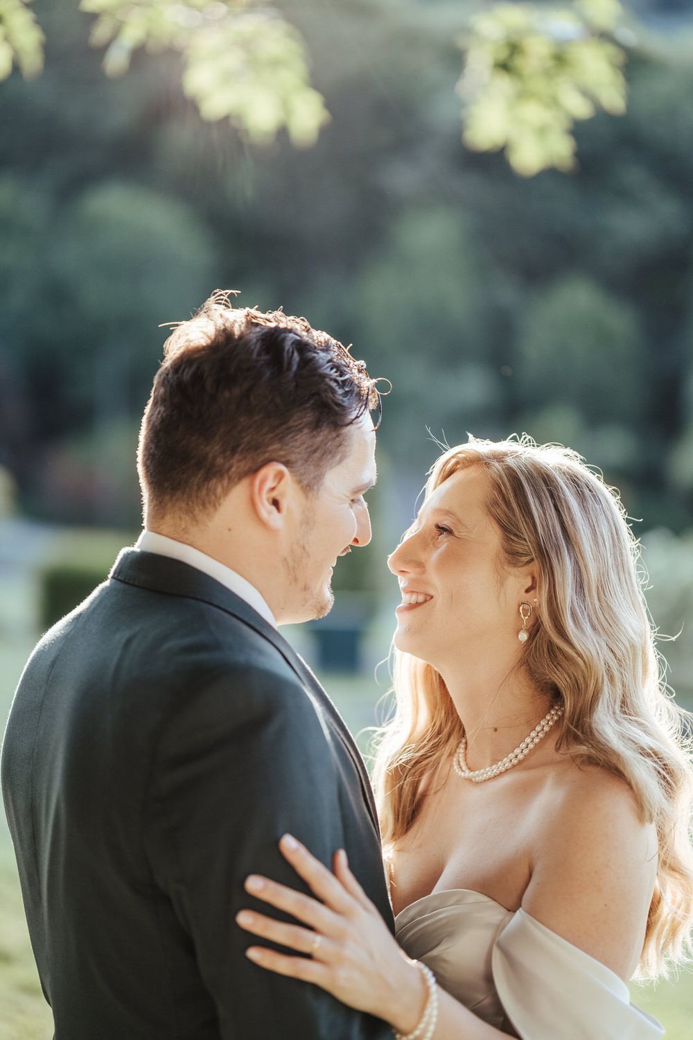 Bride and groom share a romantic smile during golden hour outdoor wedding portrait.