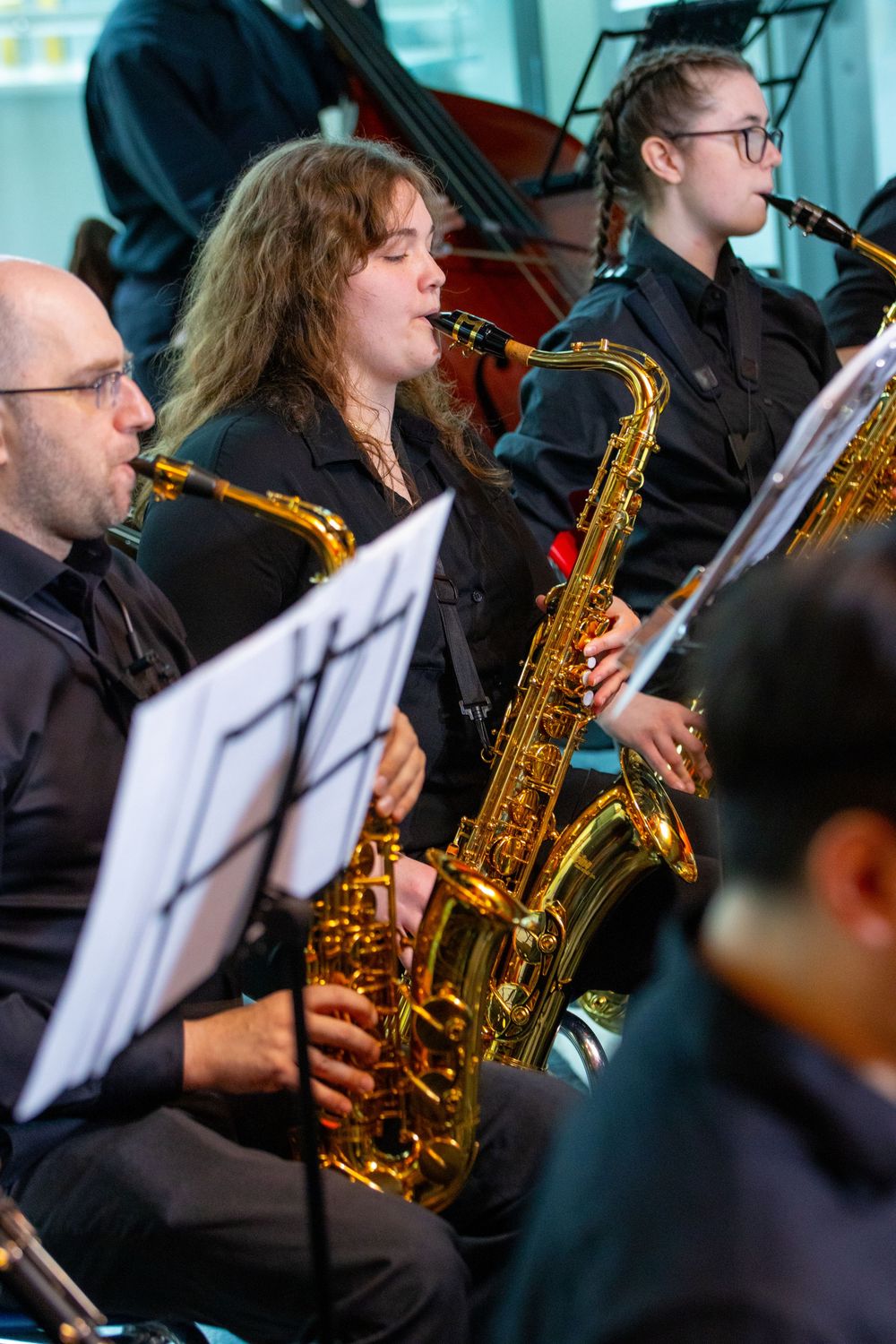 Musicians playing saxophones in a jazz ensemble, dressed in black, reading sheet music during a live performance.