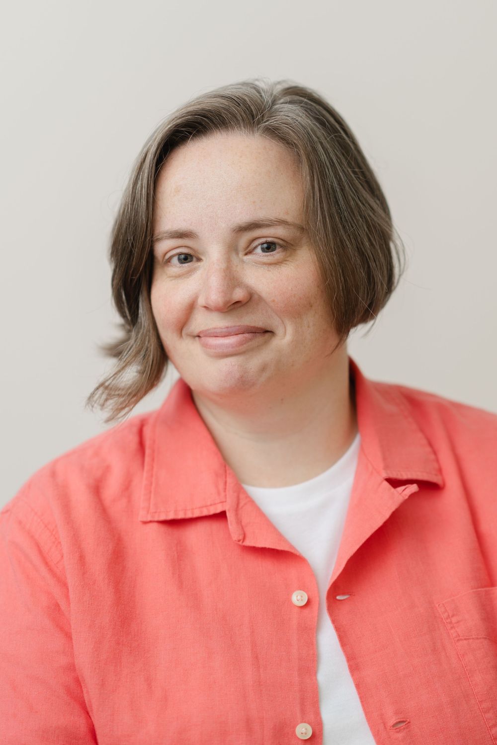 Smiling woman with short brown hair wearing a coral linen shirt in a casual professional headshot.