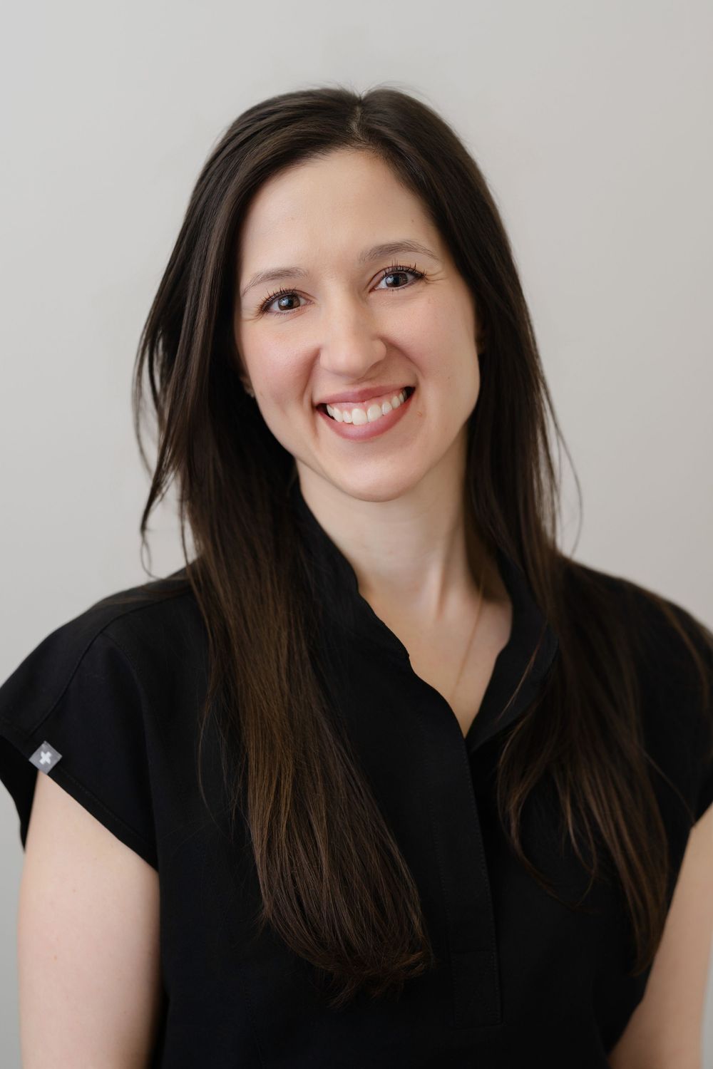 Professional headshot of a smiling woman with long dark hair wearing a black top against a light background.