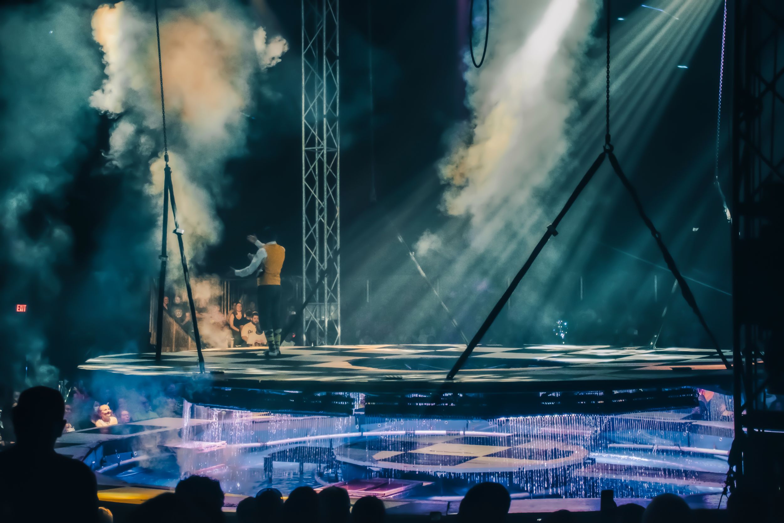 Dramatic circus stage with smoke, spotlights, and blue LED lighting during a live performance.