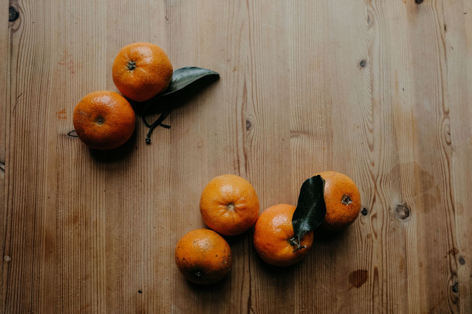 A flat lay of fresh clementines and foliage arranged on a wooden surface, captured as part of a product or lifestyle brand photography sessi