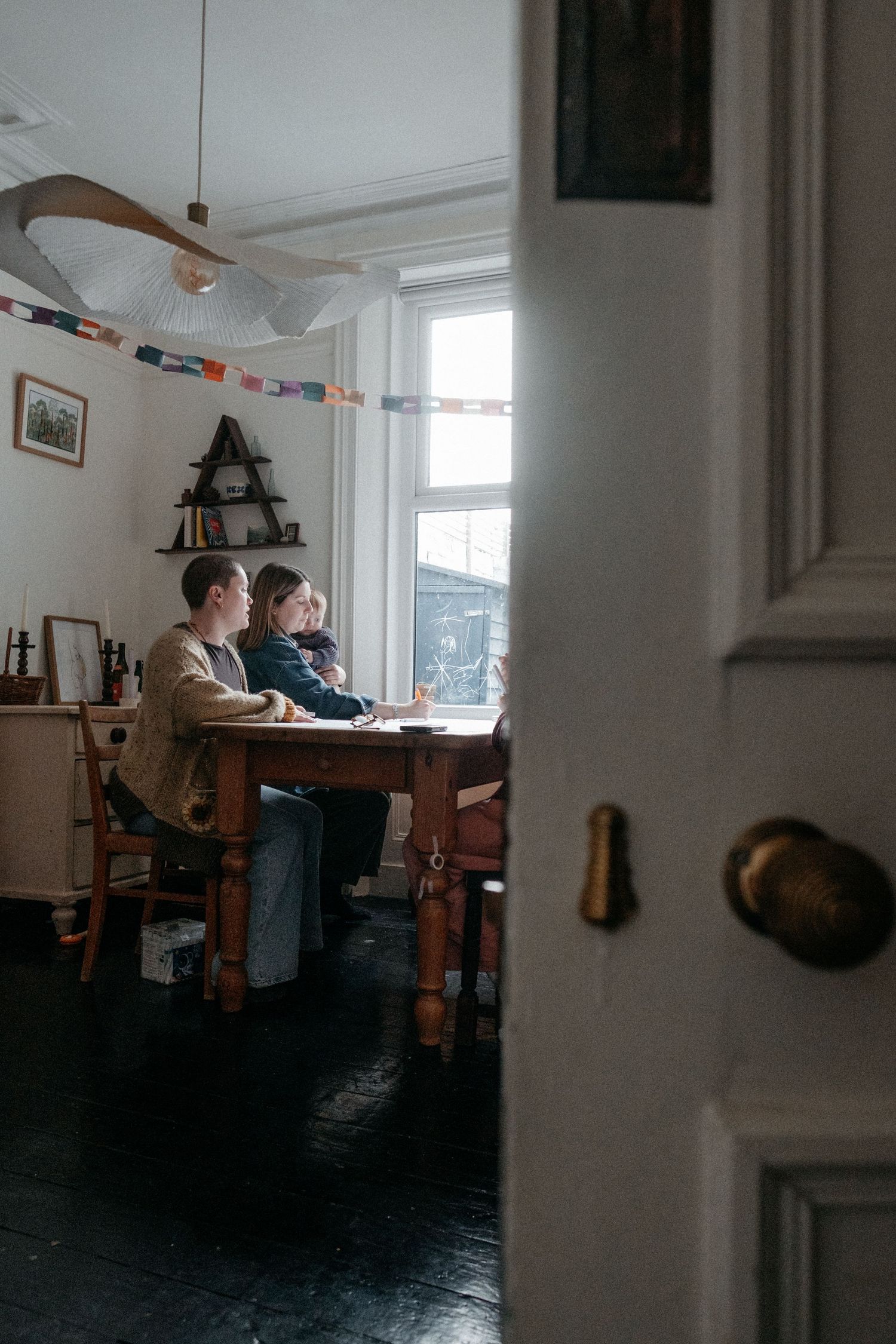 A person working alone at a dining table in a warmly lit home interior, captured in a candid lifestyle brand photography session.