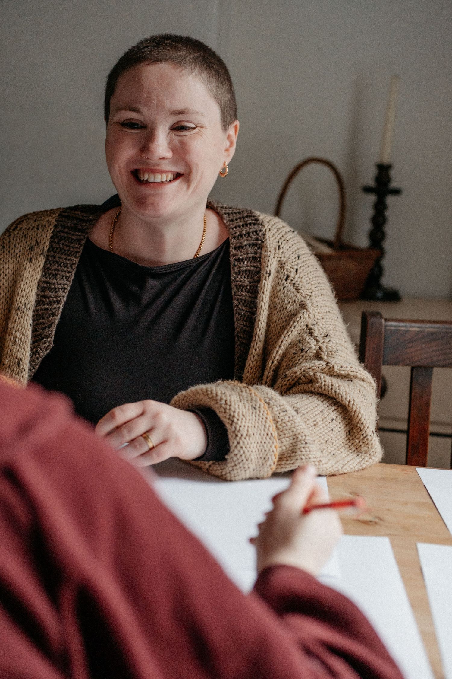 A woman smiling warmly at a wooden desk during a relaxed personal brand photography session, with soft natural light and vintage props in th