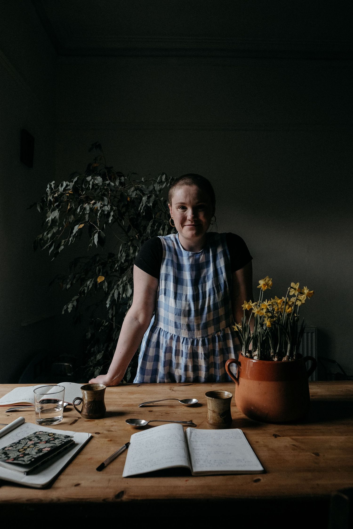 A person seated at a dark, moody workspace with an open notebook and plants, captured during a creative personal brand photography session.