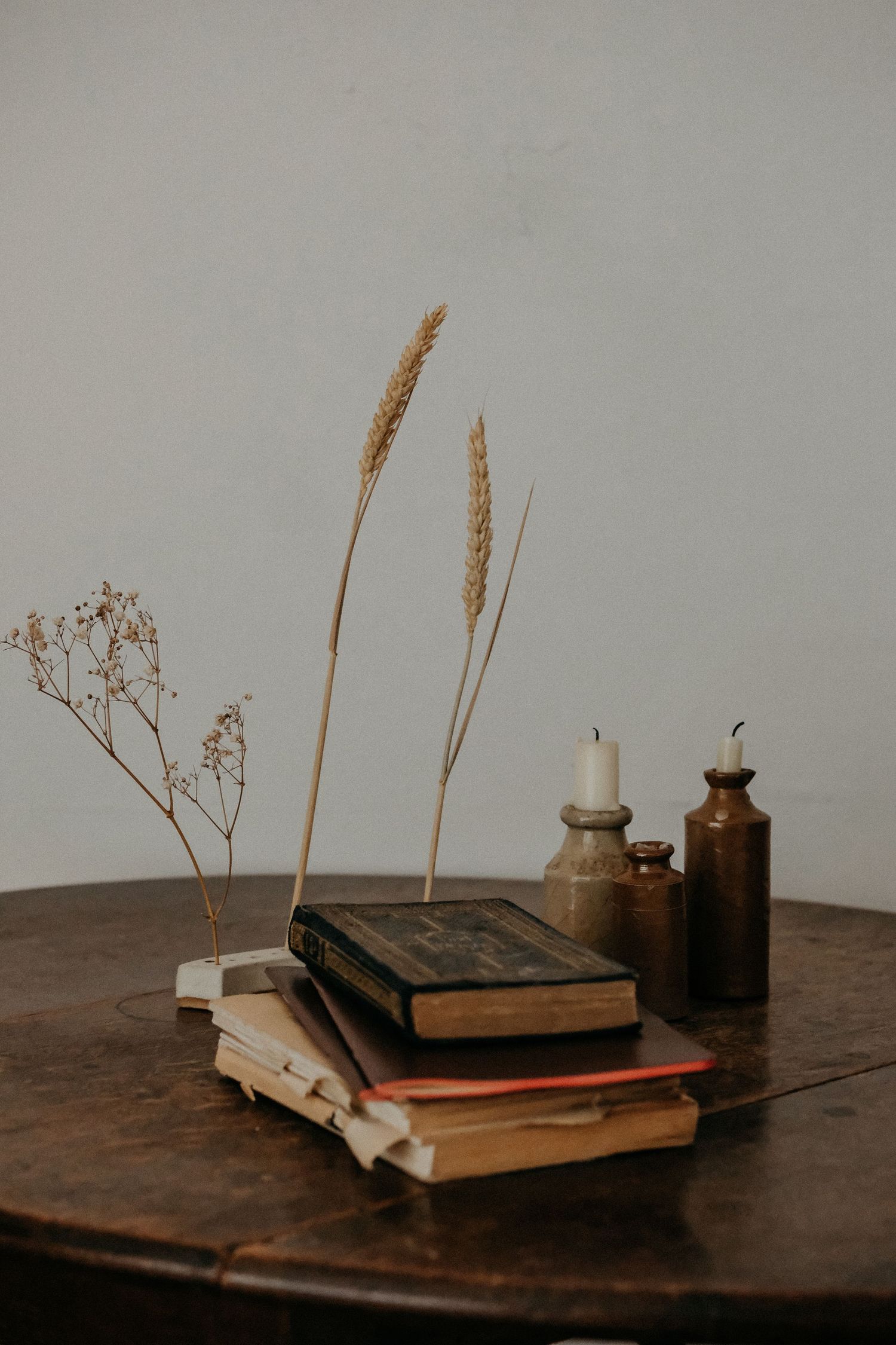 A styled flat lay of stacked books, dried pampas grass and small bottles