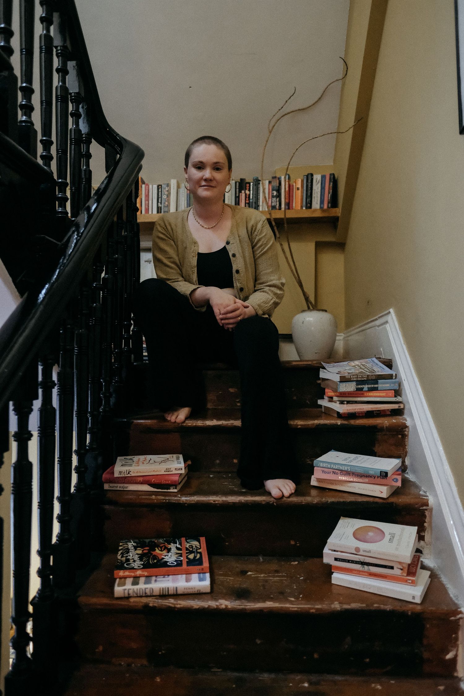 A woman sitting on a staircase surrounded by stacked books, captured in a relaxed and characterful personal brand photography session.