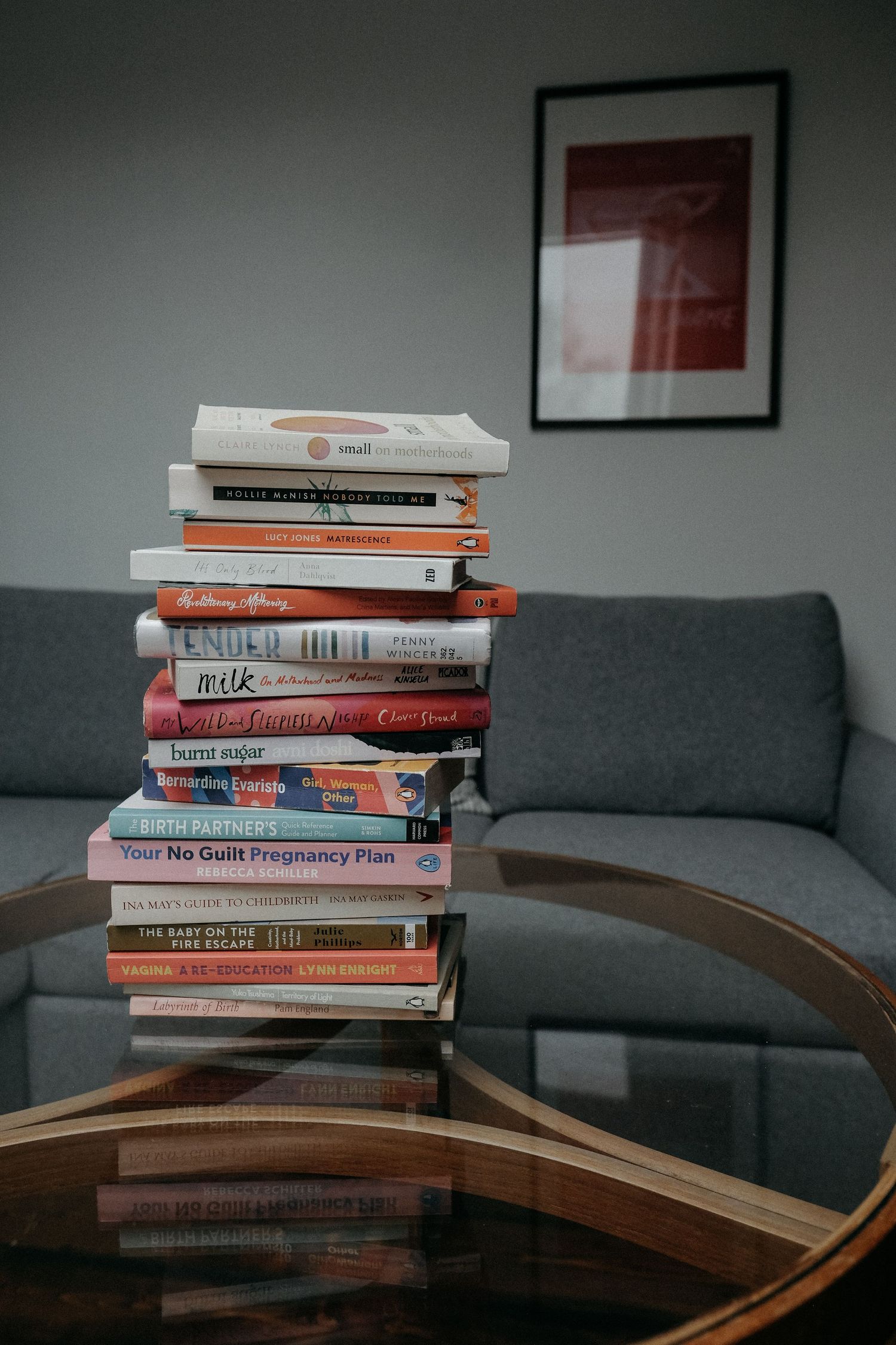 A tall stack of colourful books balanced on a chair against a dark interior backdrop, styled as part of a creative brand lifestyle photograp