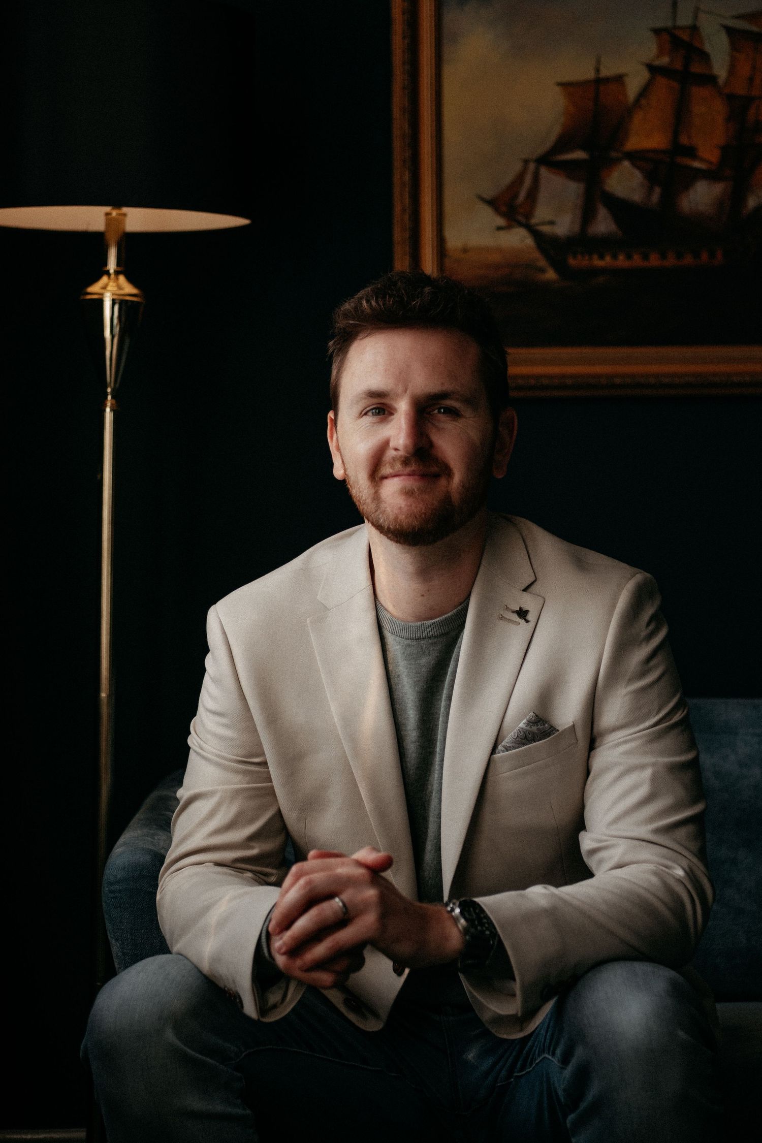 A man in a smart blazer seated in a confident, approachable pose during a professional personal brand portrait session.