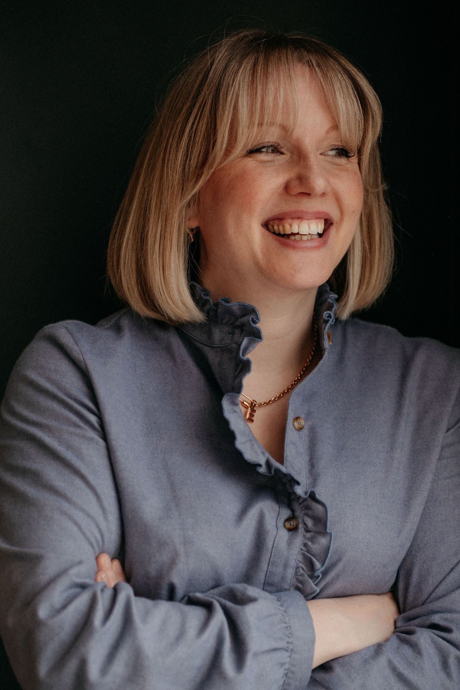 A woman with a blonde bob smiling confidently with arms crossed during a professional personal brand portrait session.
