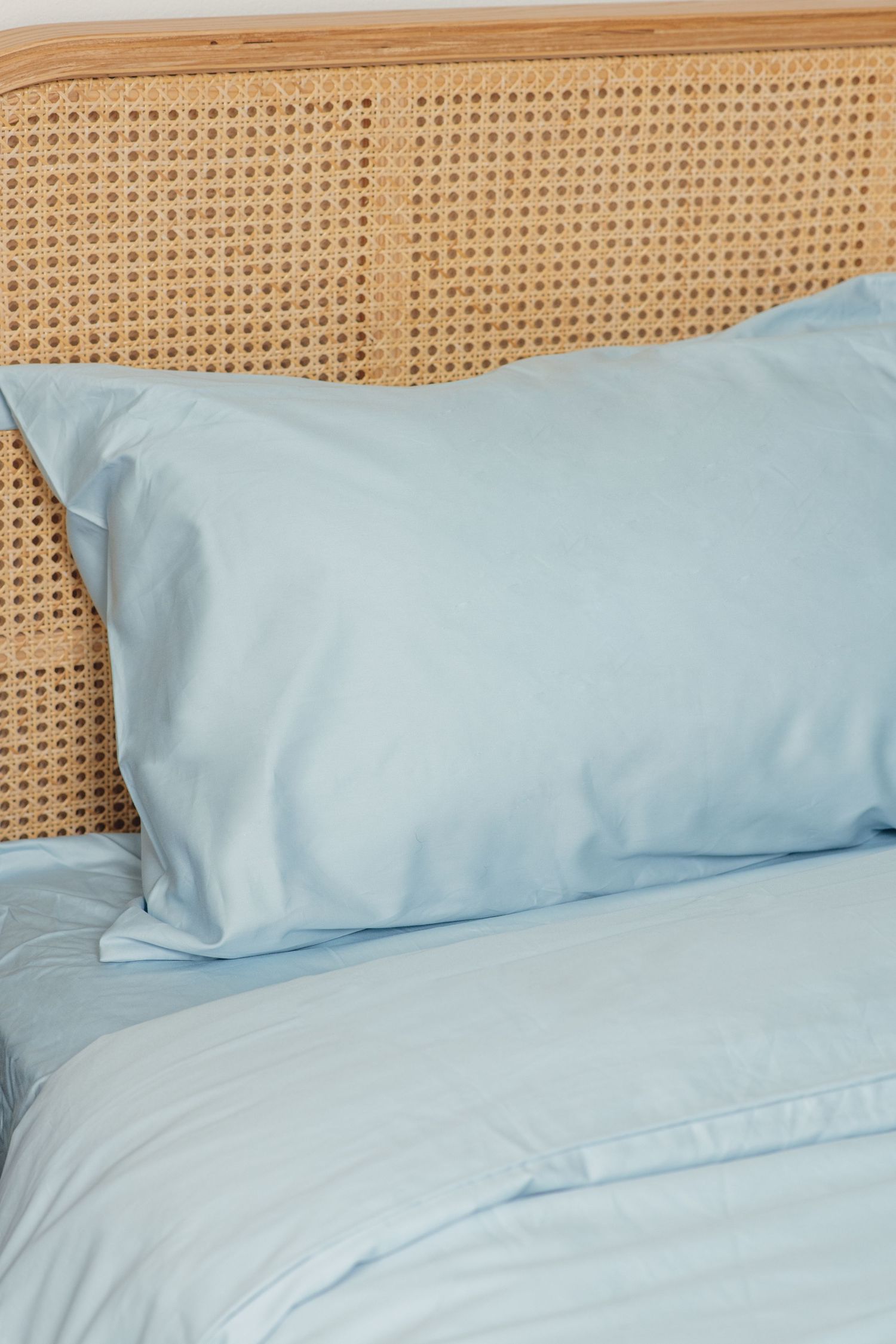 Light blue pillow and bedding set on a rattan headboard bed in a bright bedroom.