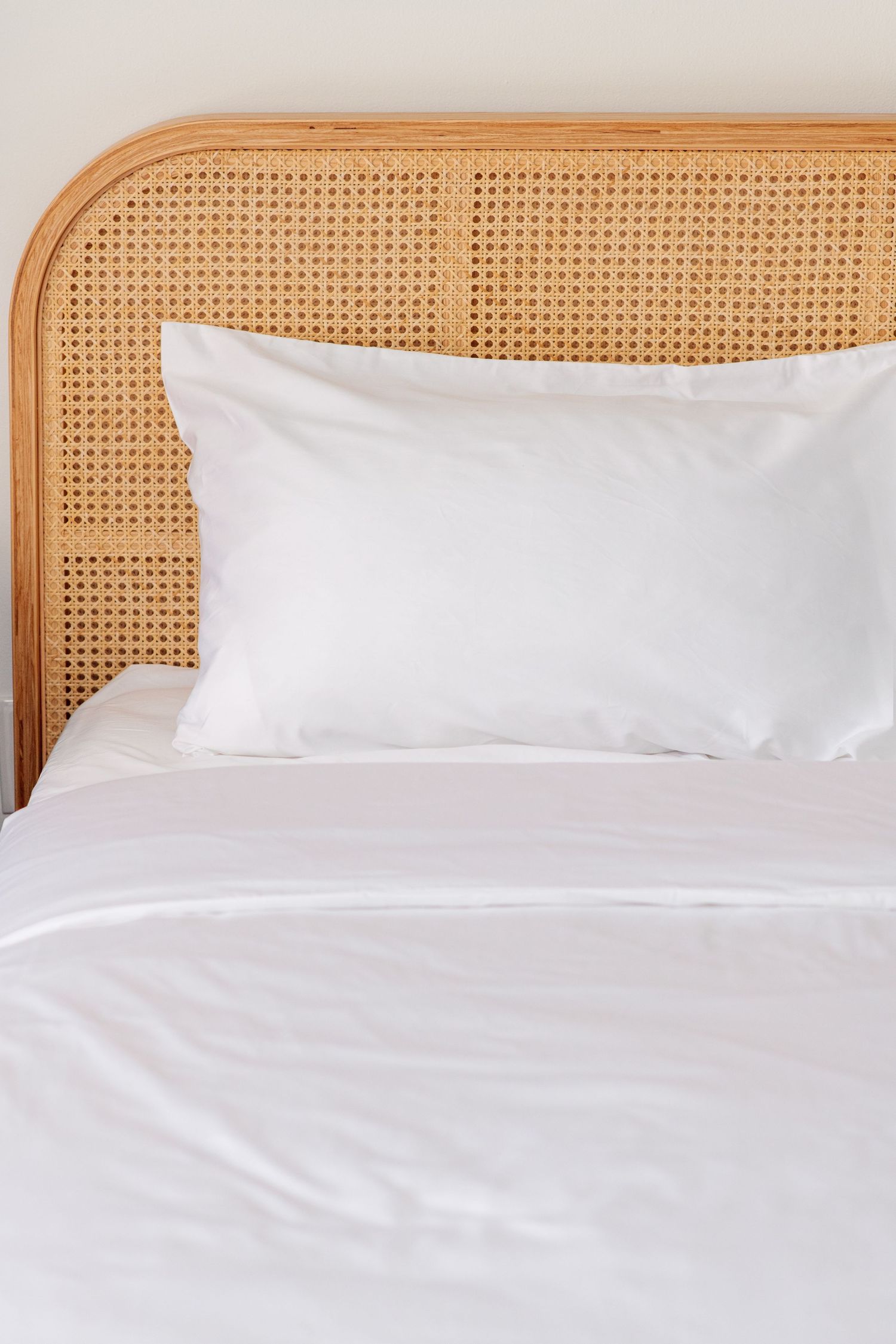White pillow and crisp white bedding on a natural rattan headboard bed frame.