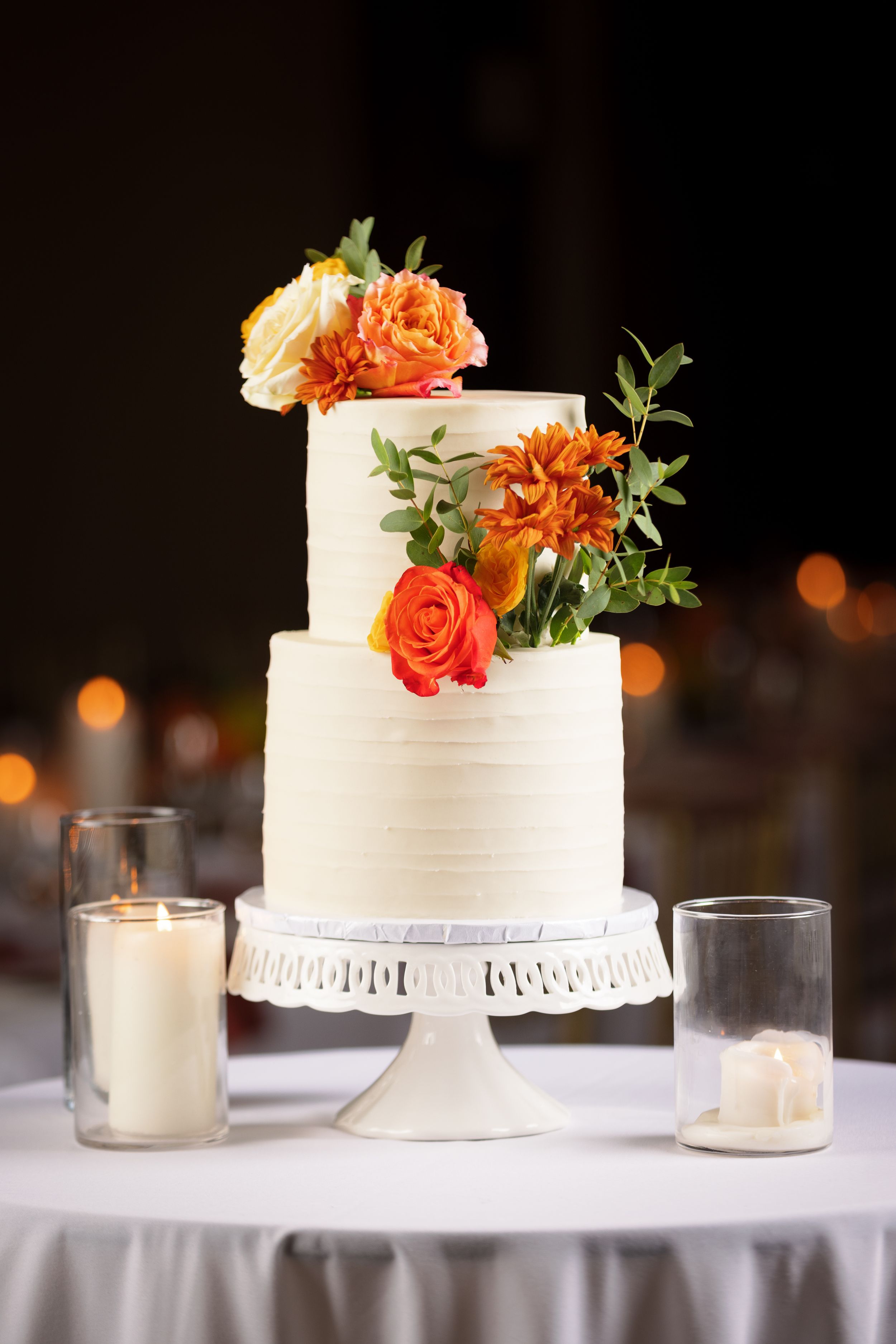 Two-tier white textured wedding cake decorated with orange and yellow flowers on white cake stand.