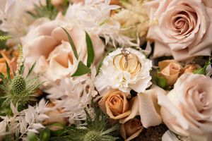 Wedding rings resting on elegant bouquet of blush roses and white flowers.