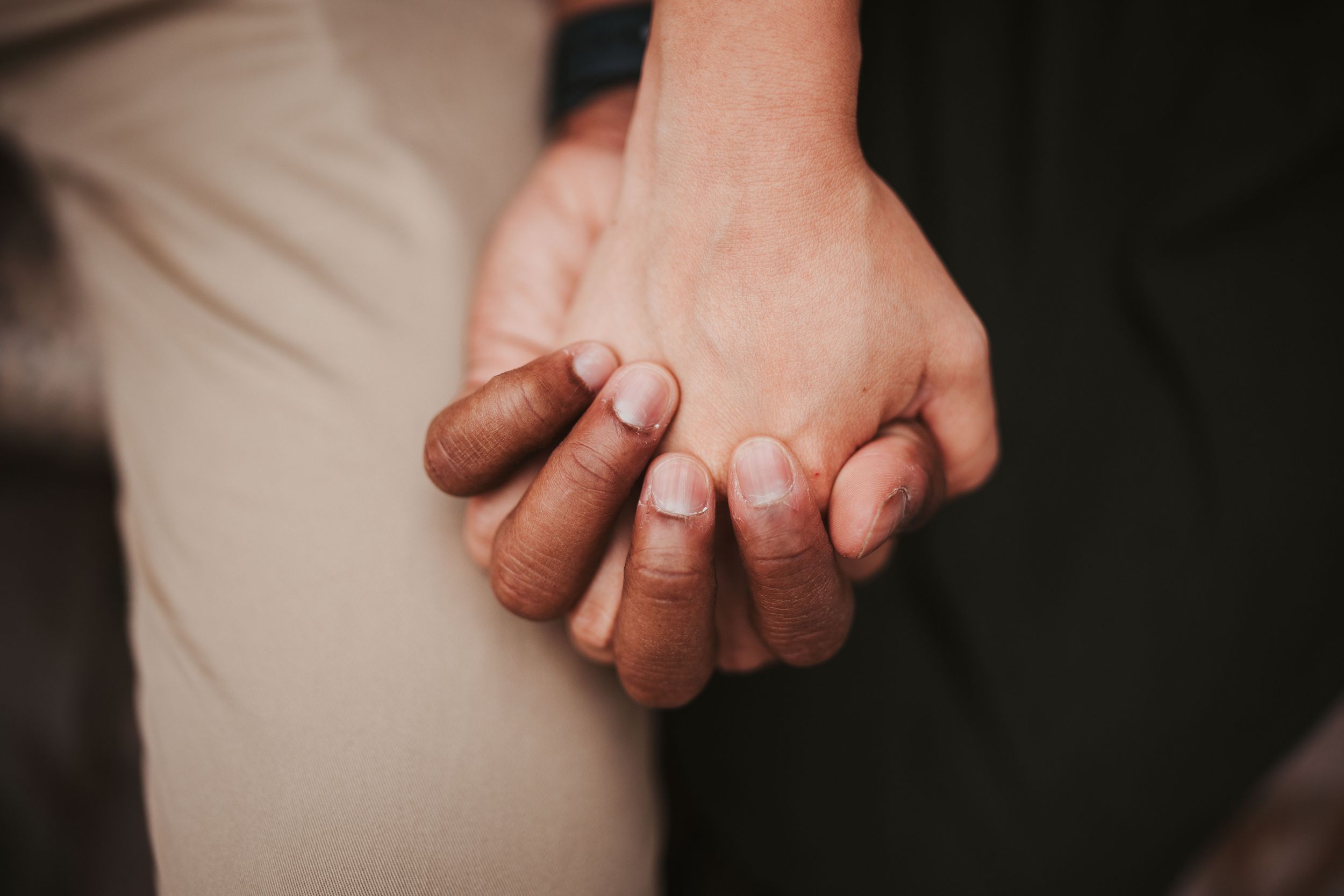 Close-up shot of two people holding hands intimately against light and dark colored clothing.