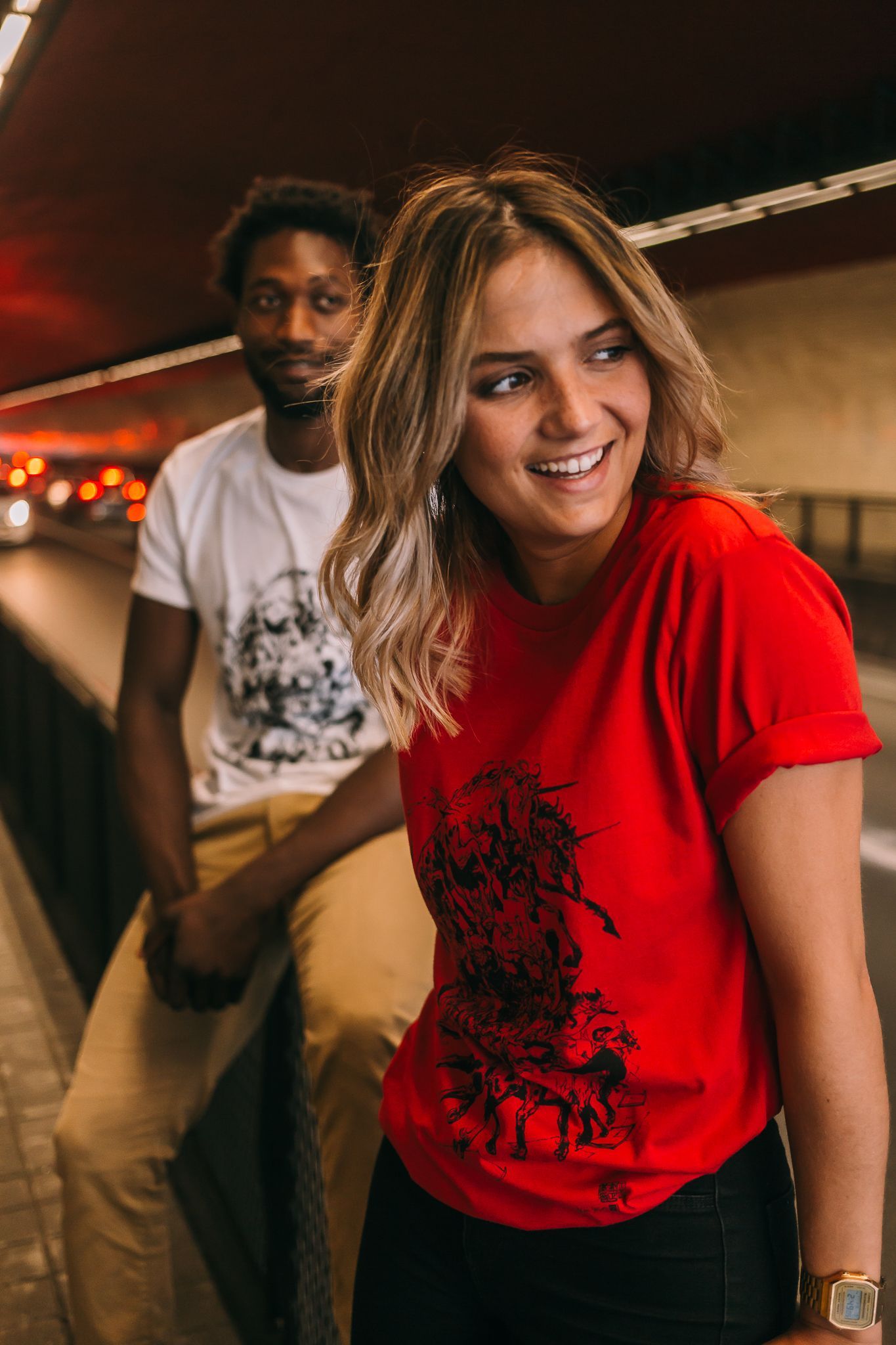 Friends hanging out in casual attire, one wearing red graphic t-shirt and another in white shirt.