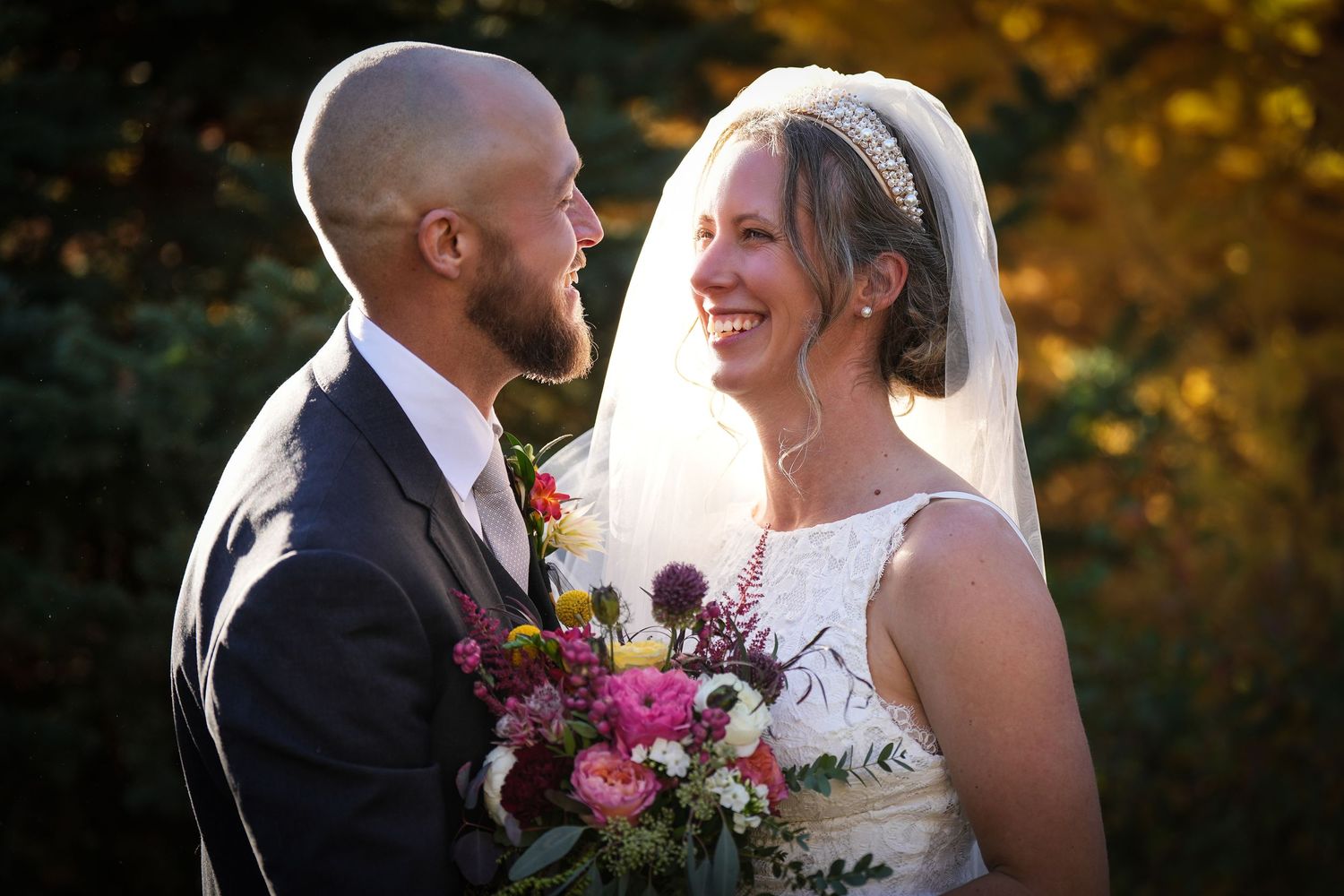 Newlywed couple sharing intimate moment outdoors with colorful autumn foliage background.