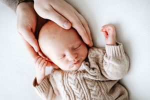 A sleeping newborn in a cozy cable knit sweater rests peacefully while gentle hands cradle their head newborn photoshoot in Nottingham